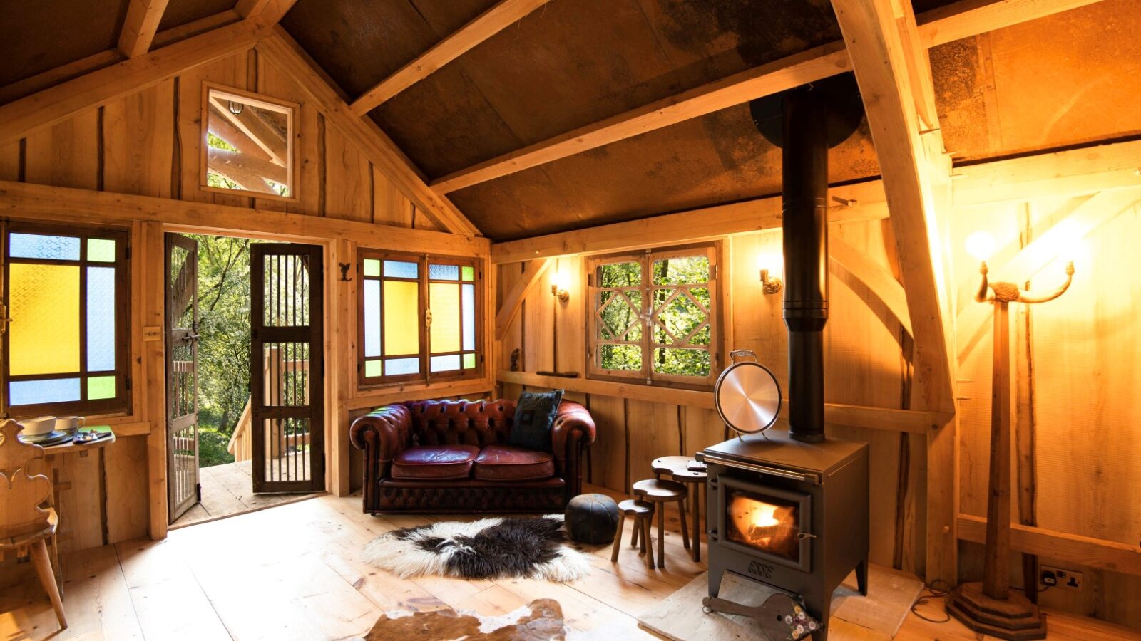 Nestled within the Arcadia landscape, this cozy cabin interior features a leather sofa, wood stove, and colorful windows. Natural wood beams and floors add rustic charm reminiscent of Westley Farm's timeless beauty.