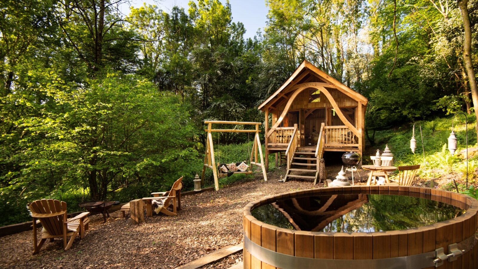 Nestled in Arcadia, this charming wooden cabin at Westley Farm is enveloped by towering trees. It features a cozy swing, inviting chairs, and a round outdoor hot tub—perfect for relaxing in the serene forest setting.