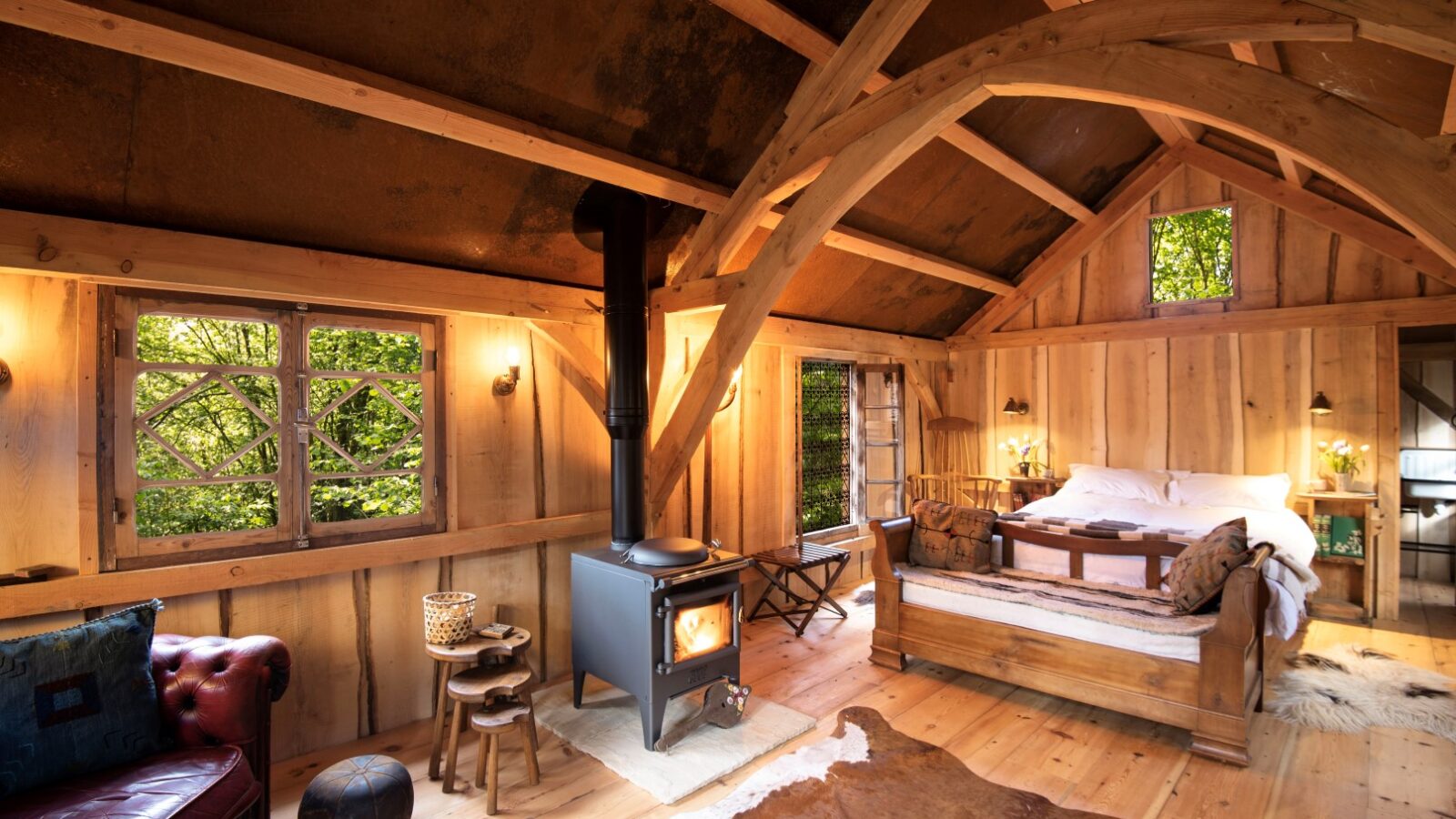 Nestled within Westley Farm, this cozy rustic cabin boasts a wood-burning stove, comfortable bed and sofas, and charming wooden furniture. Large windows frame the lush greenery outside, creating an Arcadian retreat for those seeking tranquility and natural beauty.