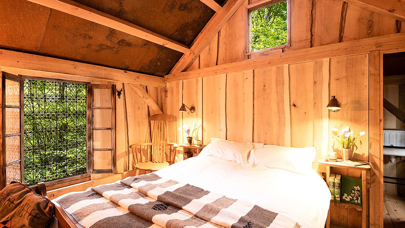 Cozy wooden cabin bedroom at Westley Farm, featuring a large bed with a plaid blanket, small windows, and soft lighting that exudes Arcadia charm.