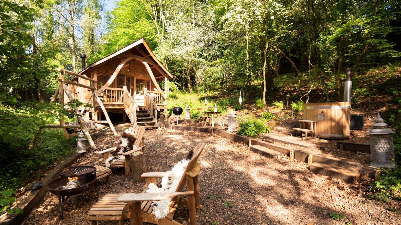 Nestled in the heart of Westley Farm, this wooden cabin offers a tranquil forest setting with outdoor seating and a cozy fire pit. Surrounded by trees and set against a clear sky, it's an Arcadia escape for nature lovers.