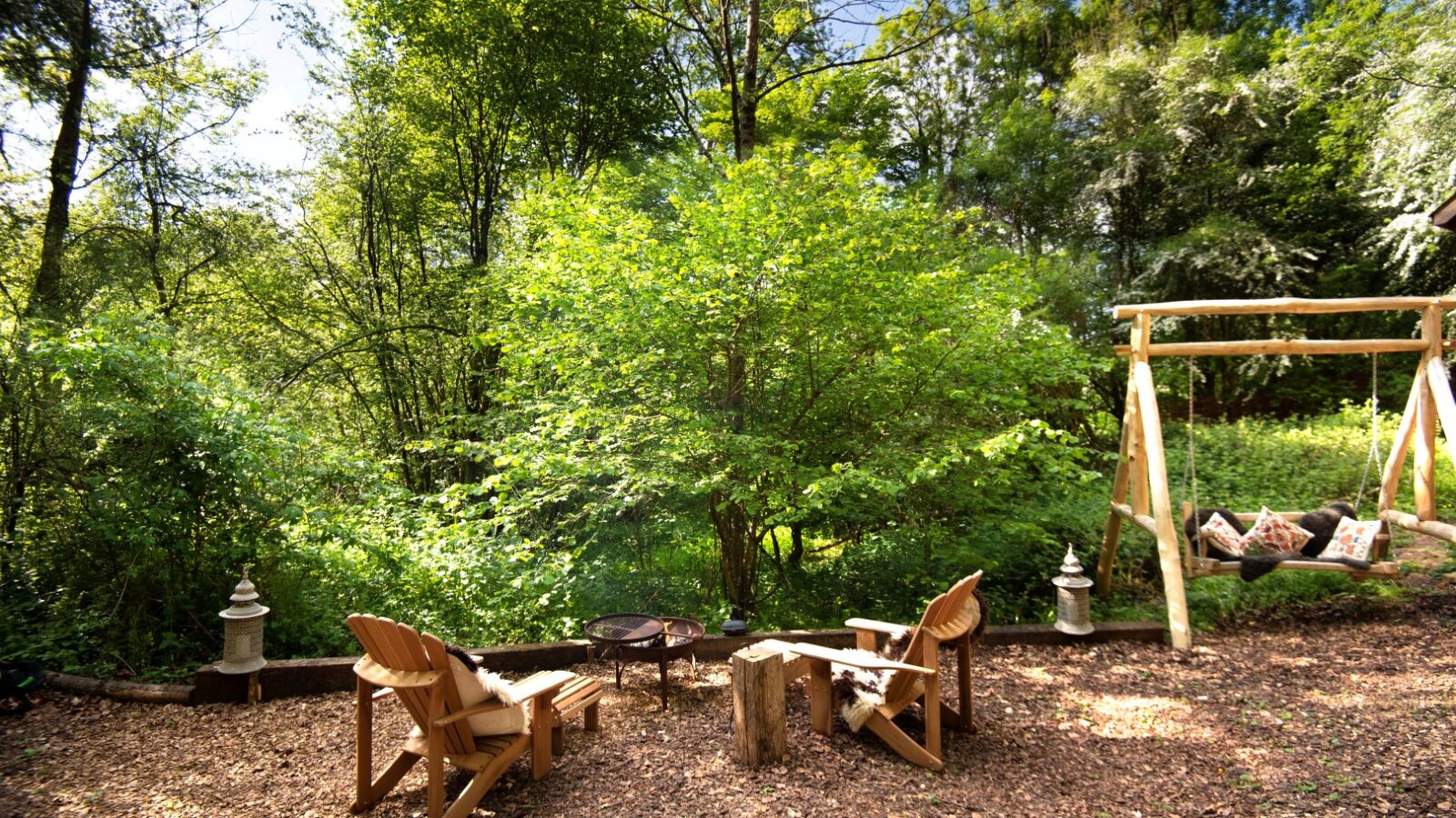 In the heart of Arcadia, wooden chairs and a swing set gather in a forest clearing at Westley Farm. A fire pit crackles amid the lush greenery, illuminated by decorative lanterns—a perfect farm retreat surrounded by nature’s tranquility.