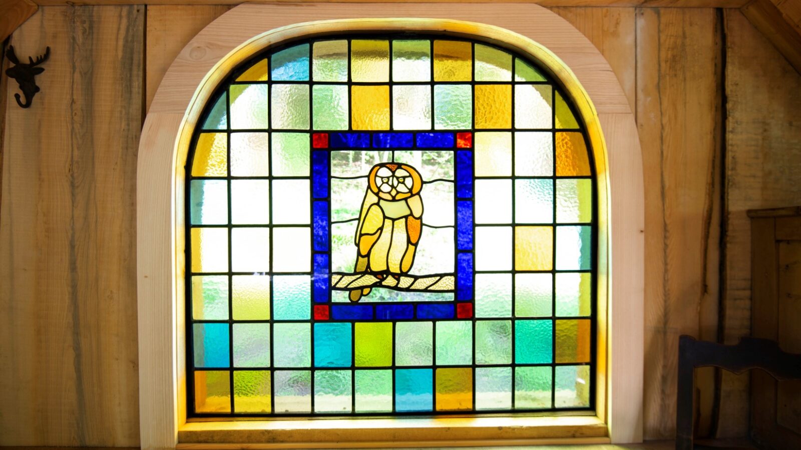 Stained glass window with colorful geometric patterns featuring an owl in the center, framed by the rustic charm of Westley Farm's wooden walls.