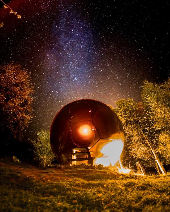 A glowing sphere-shaped structure under a starry night sky, surrounded by trees and illuminated from within, captures the essence of Chillderness. This enchanting spot offers a unique glamping experience where nature and tranquility seamlessly blend.