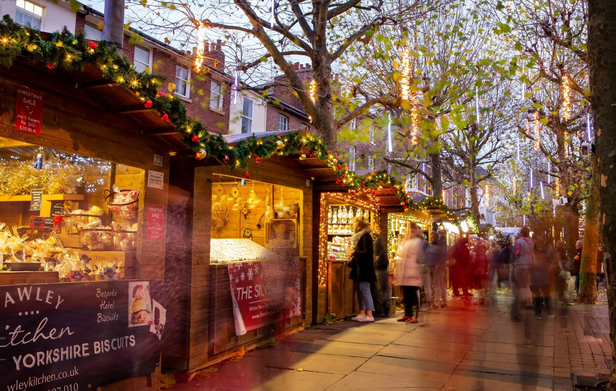 People browsing wooden stalls at one of the best Xmas markets in the UK, adorned with festive holiday lights during twilight.