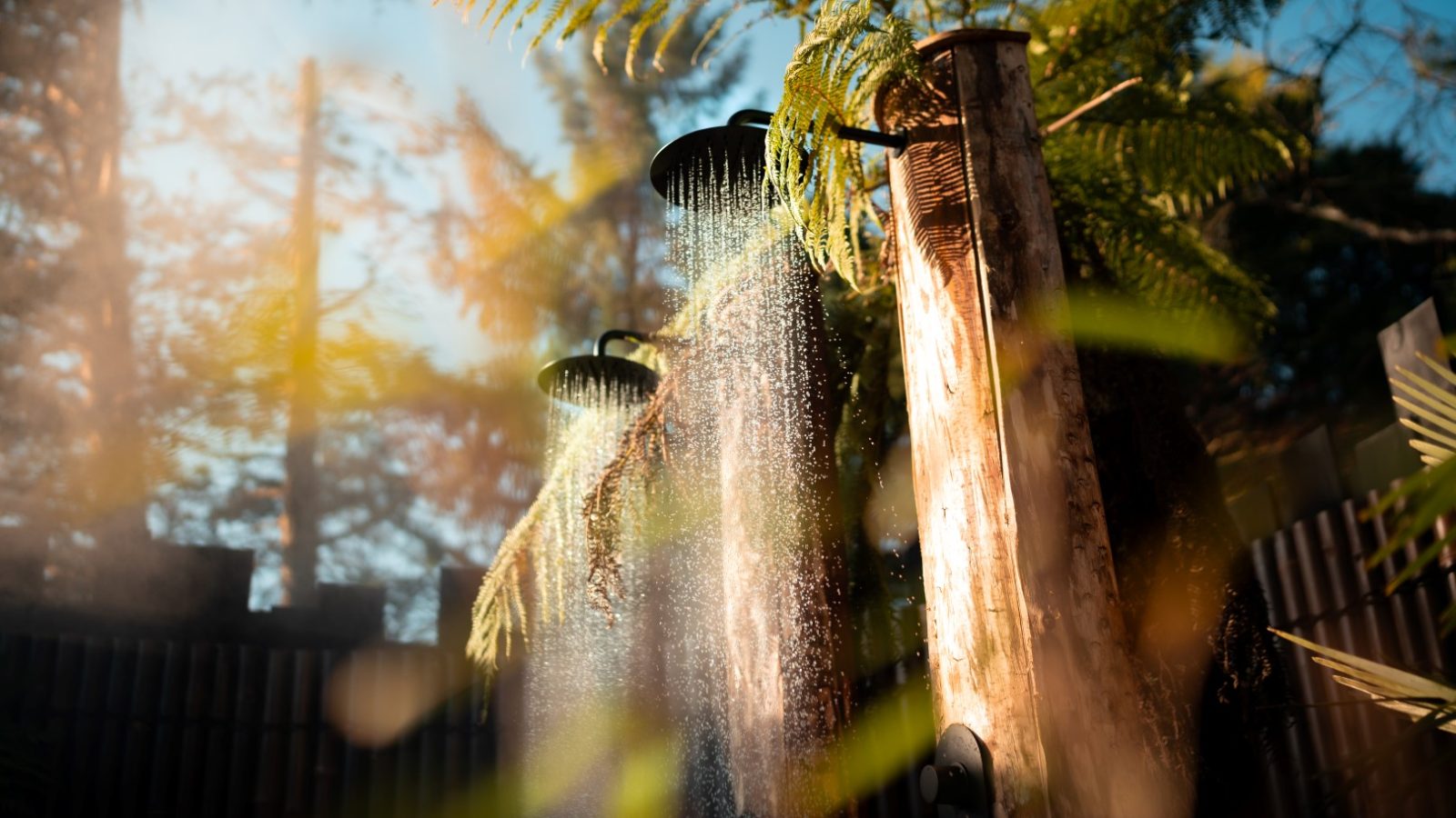 An outdoor shower with water flowing, surrounded by fern leaves and wooden posts, like a haven in Fenny Castle.