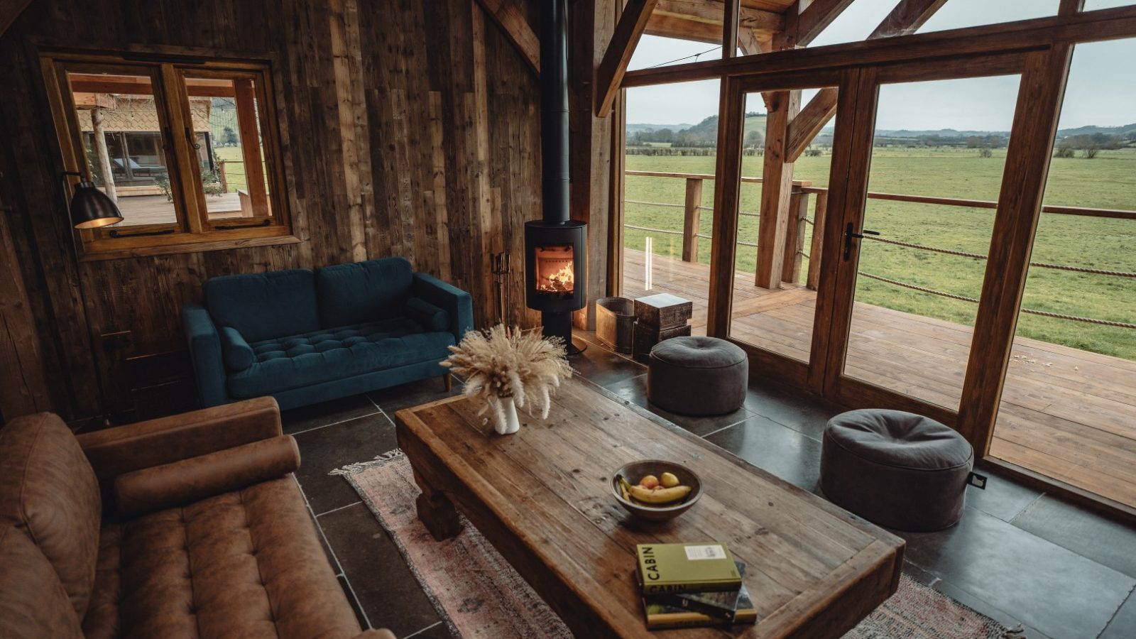 Cozy cabin interior with wooden decor, a fireplace, blue and brown sofas, and a large window overlooking Fenny Castle.