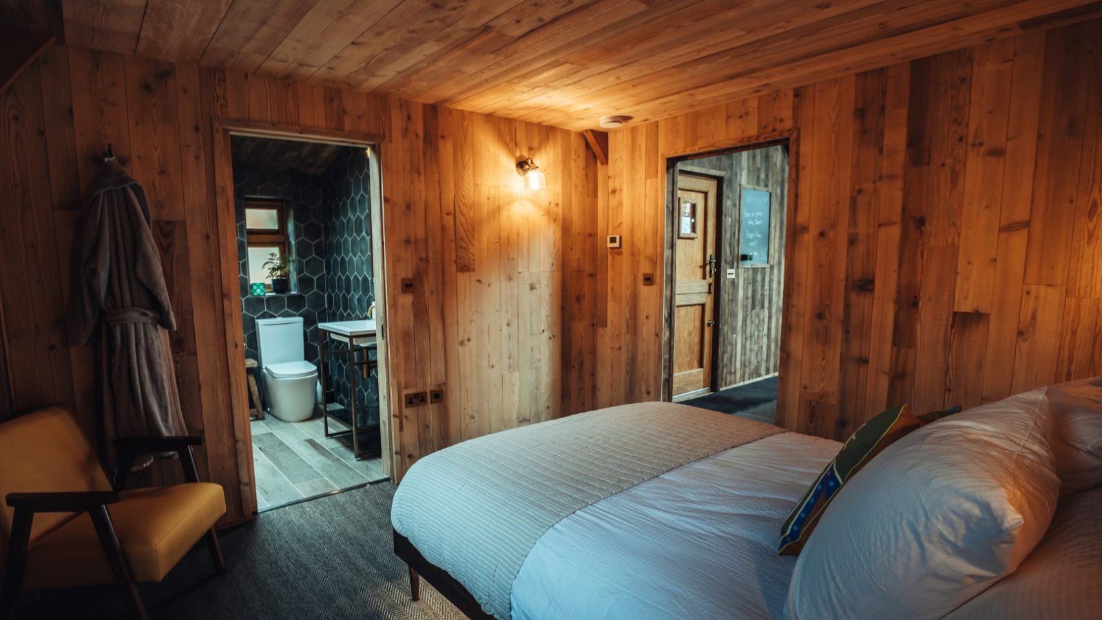 A cozy wooden bedroom with a double bed, nestled near Fenny Castle, featuring doorways to a bathroom and another area.