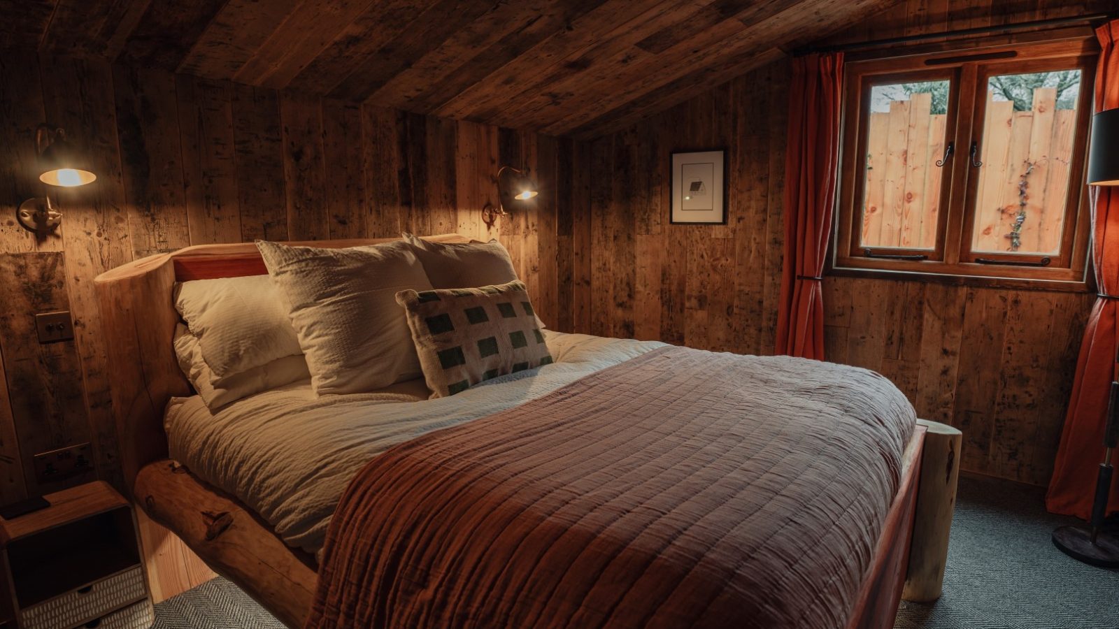 Rustic bedroom with wooden accents, a cozy bed, two lamps, and a window overlooking Fenny Castle.