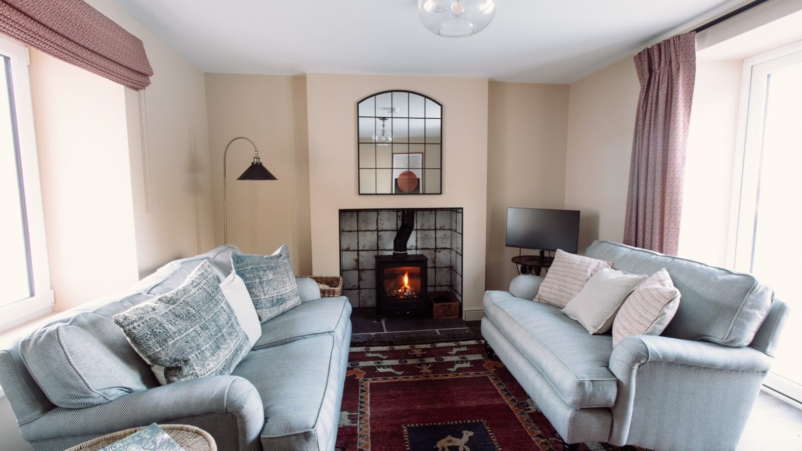 Cosy living room at Cleugh Foot with two sofas, a lit fireplace, a mirror above, a small TV, and a patterned rug on the floor.