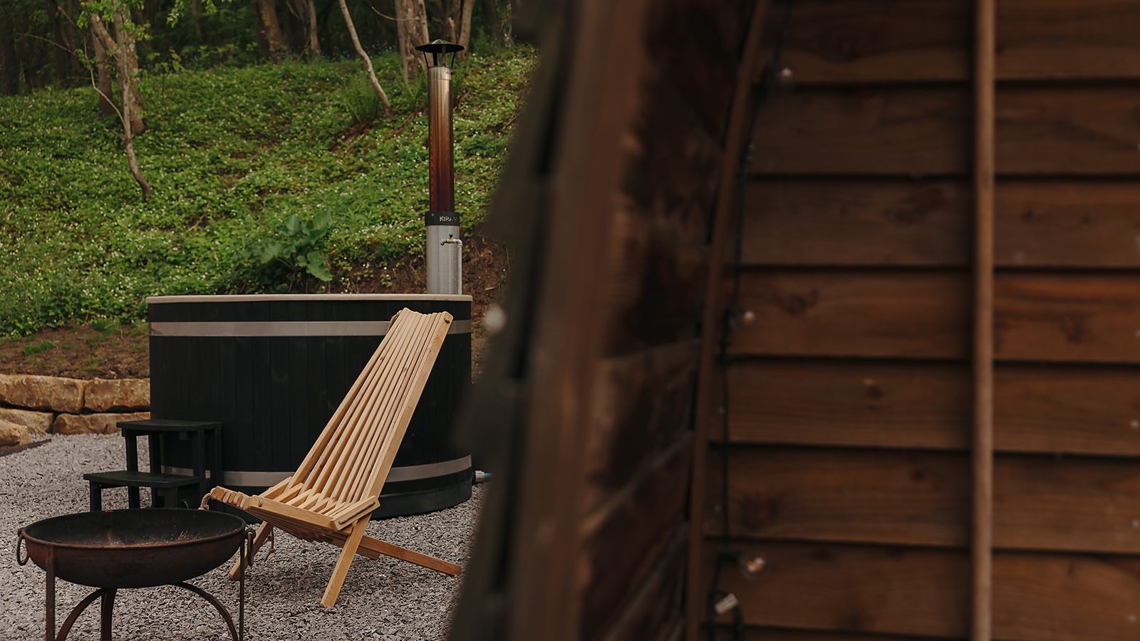 A hewn wooden chair and metal fire pit sit invitingly near the hot tub in the serene, wooded setting of Yorkshire.