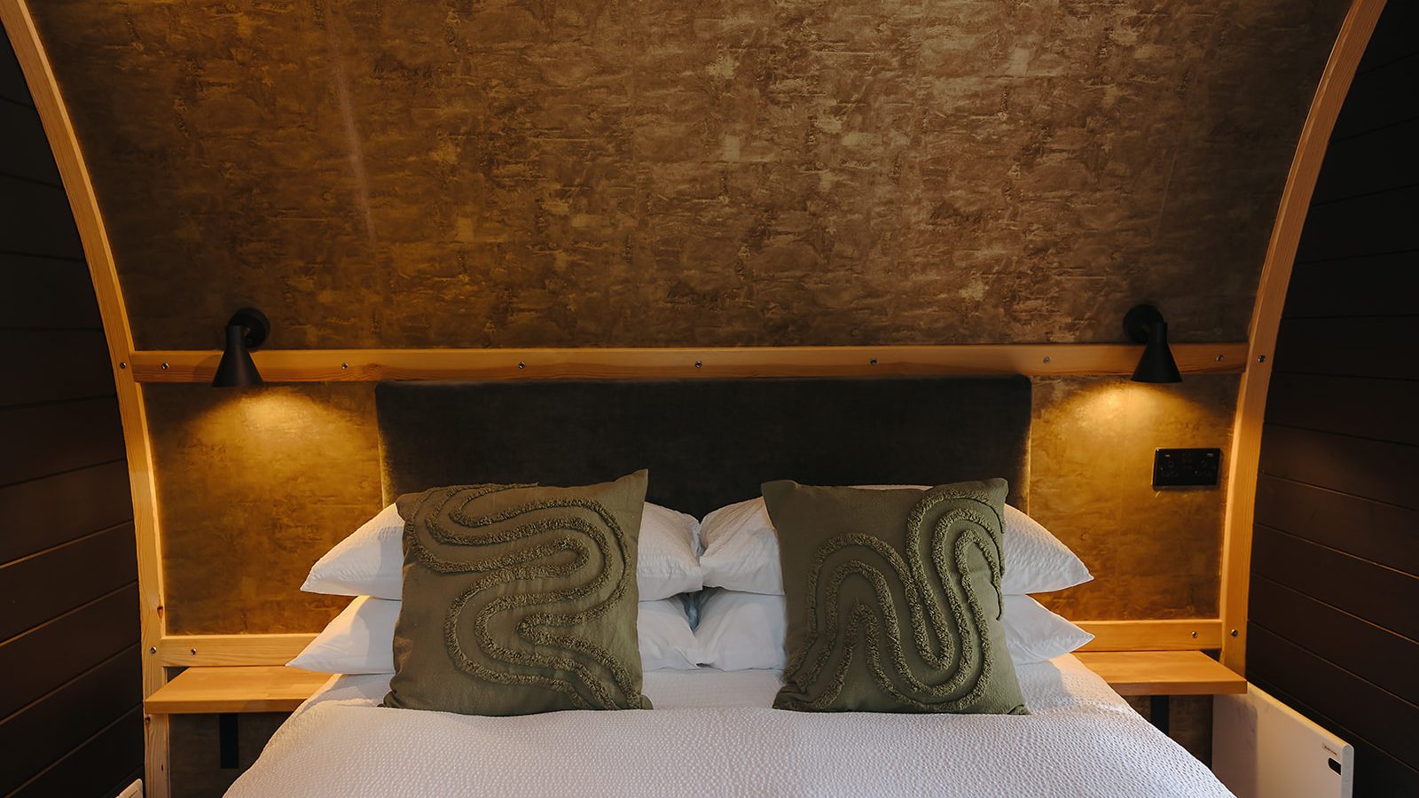 Cozy Yorkshire bedroom featuring a hewn wooden headboard, two green pillows, white bedding, and warm ambient lighting on each side.