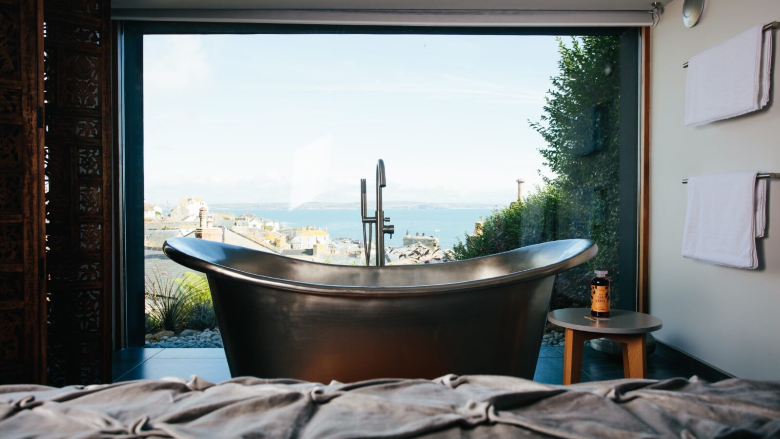 A luxurious bathroom with a freestanding metal bathtub offers a fallen angel's view of the scenic coast through a large window.