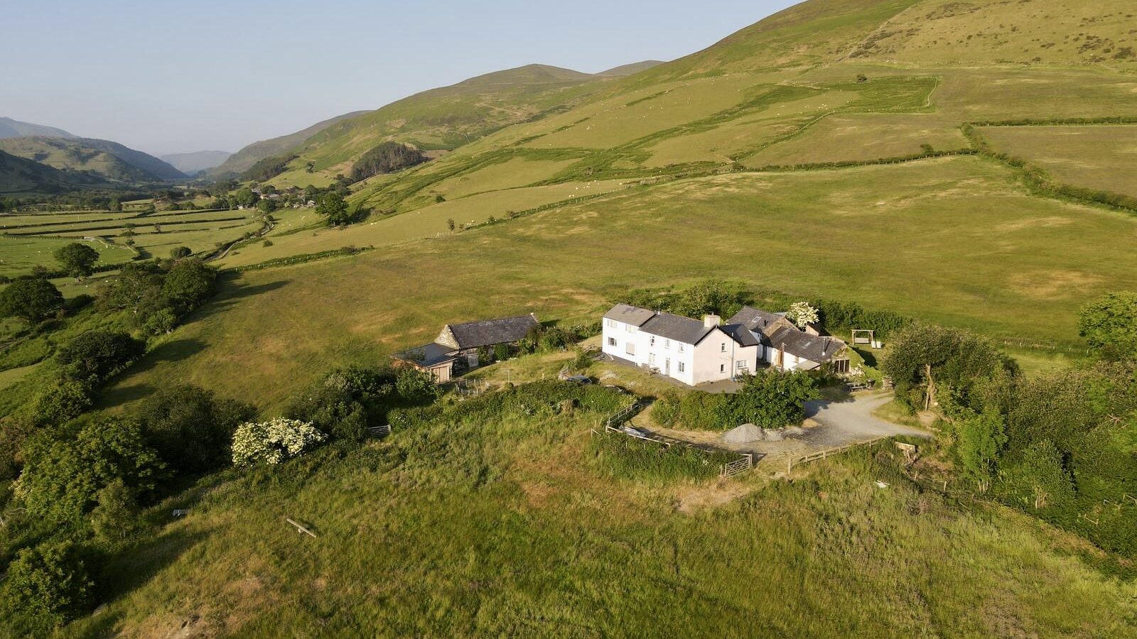 Aerial view of a white house, a perfect hideaway nestled among fields and rolling hills under the clear sky of Snowdonia.