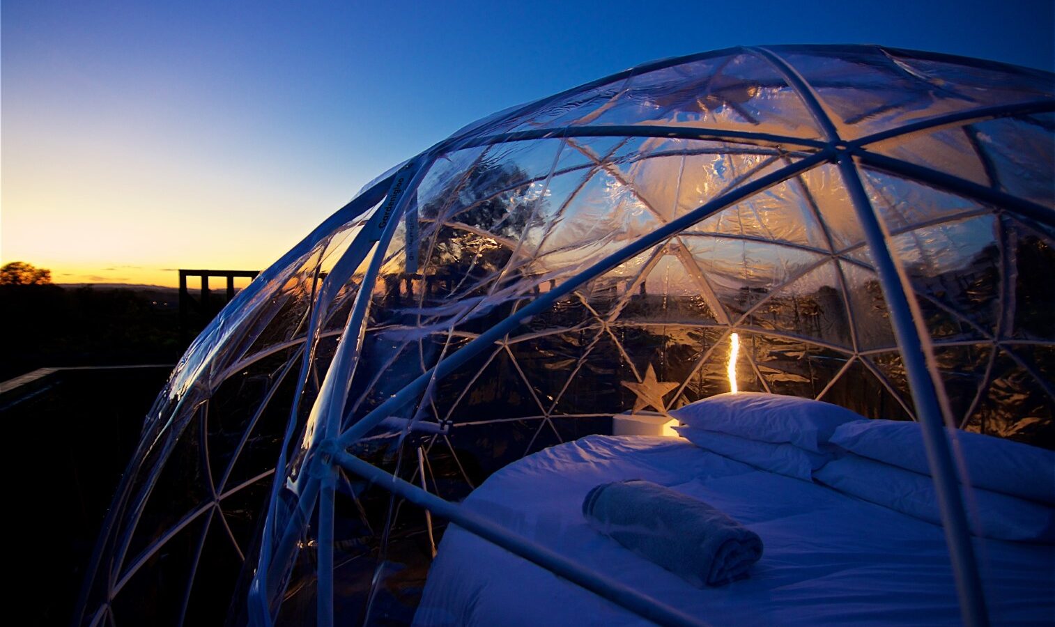 Experience the enchanting views of the surrounding landscape and evening sky from Georges Getaway's transparent dome tent, complete with a cozy bed inside for a perfect sunset retreat.