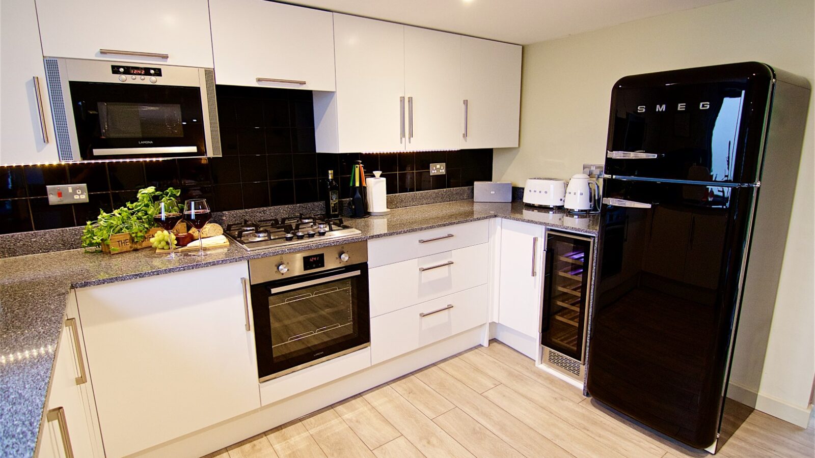 Georges Getaway features a modern kitchen with white cabinets, a sleek black backsplash, stainless steel appliances, and a striking black Smeg refrigerator.