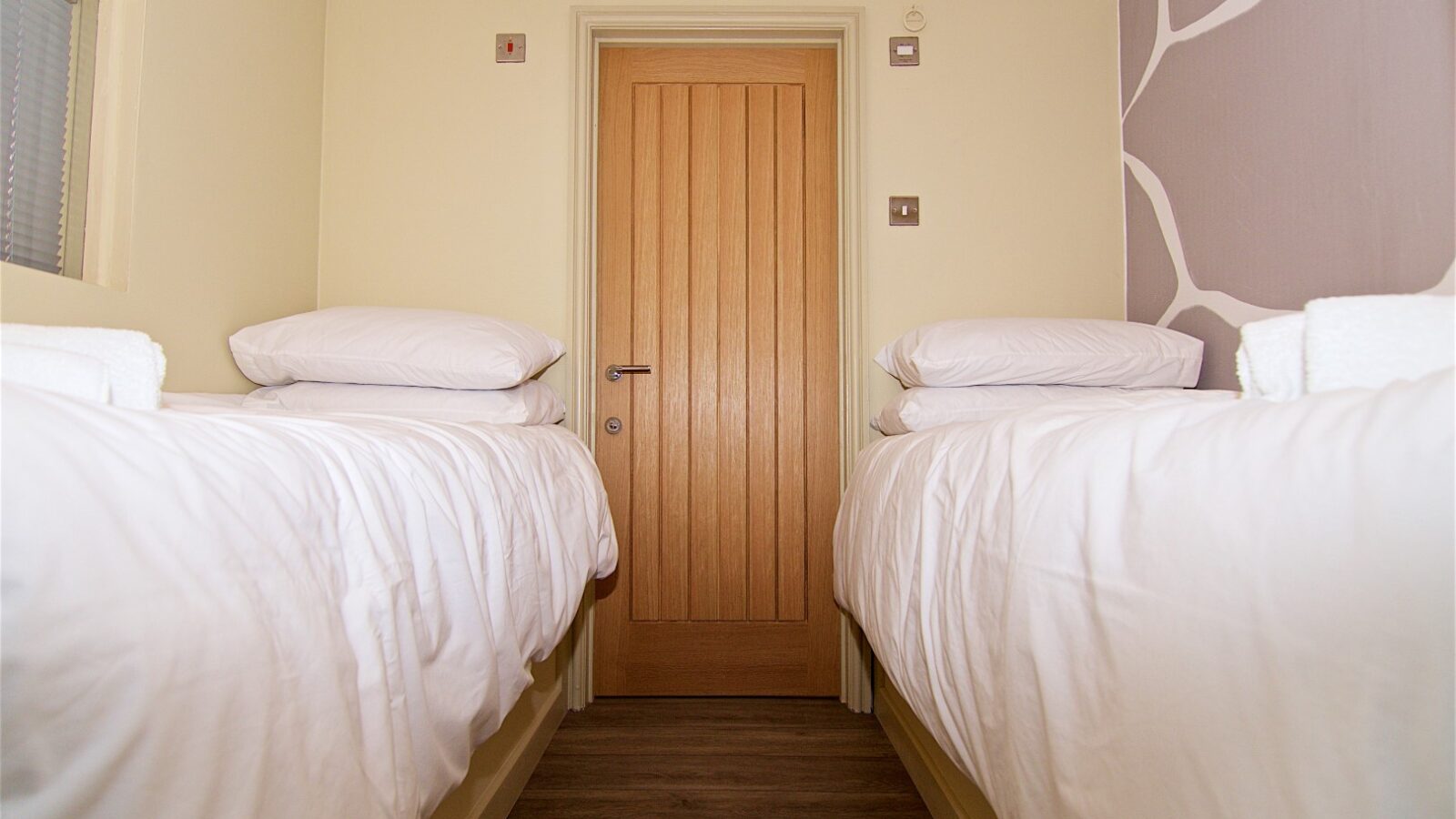 Two single beds with white bedding are placed opposite each other in a small room at Georges Getaway, featuring a wooden door and minimalist decor.