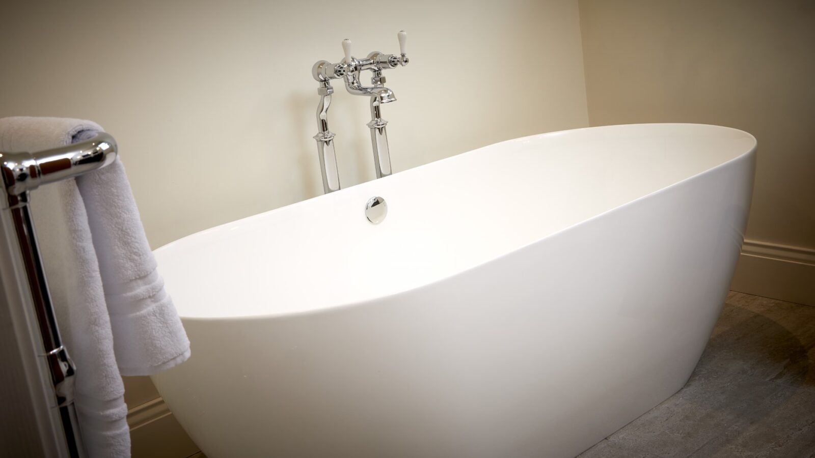 The freestanding white bathtub with a chrome faucet, accompanied by a towel on a nearby rack, evokes the elegance of equestrian stables, set against a soothing cream-colored wall.