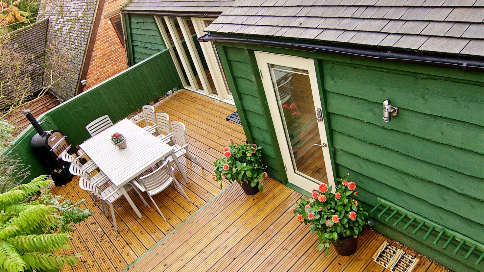 Aerial view of Georges Getaway showcases a wooden deck with a table, chairs, two potted plants, and a green building with a glass door—a perfect retreat.