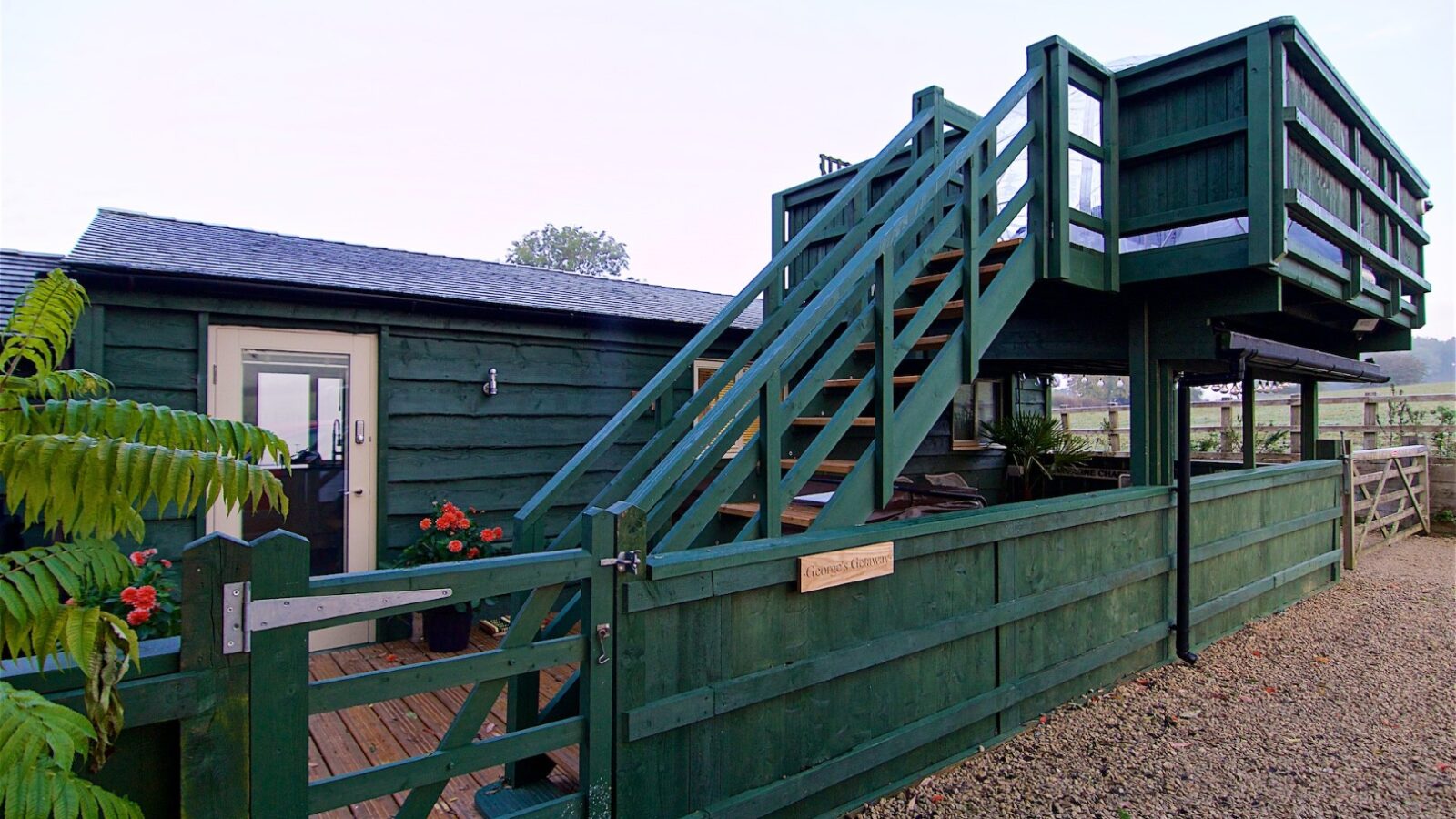 A wooden outdoor staircase guides you to Georges Getaway, a raised deck area beside a green-painted building with a gravel path and lush plants.