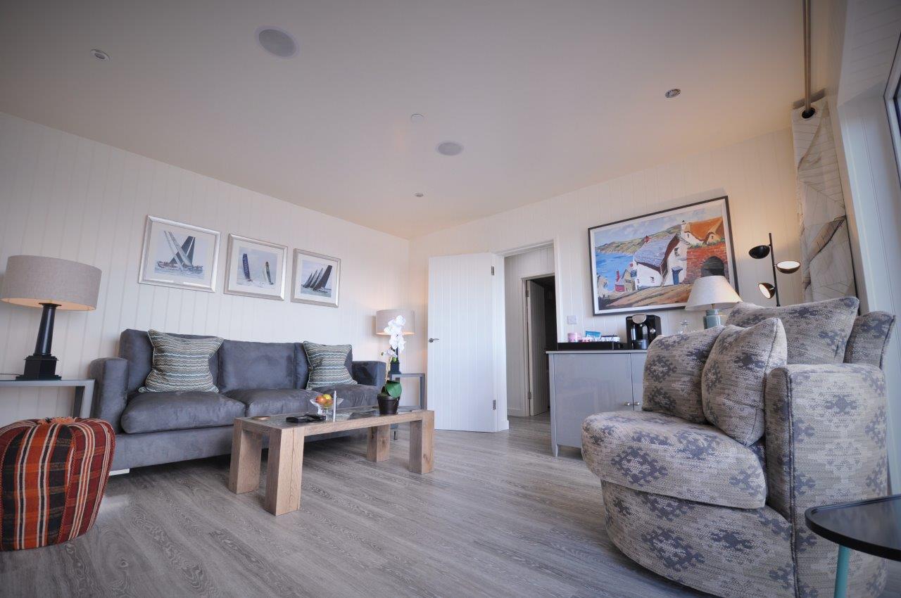 A modern living room with a gray sofa, patterned armchairs, a wooden coffee table, and decorative wall art reminiscent of beach huts.