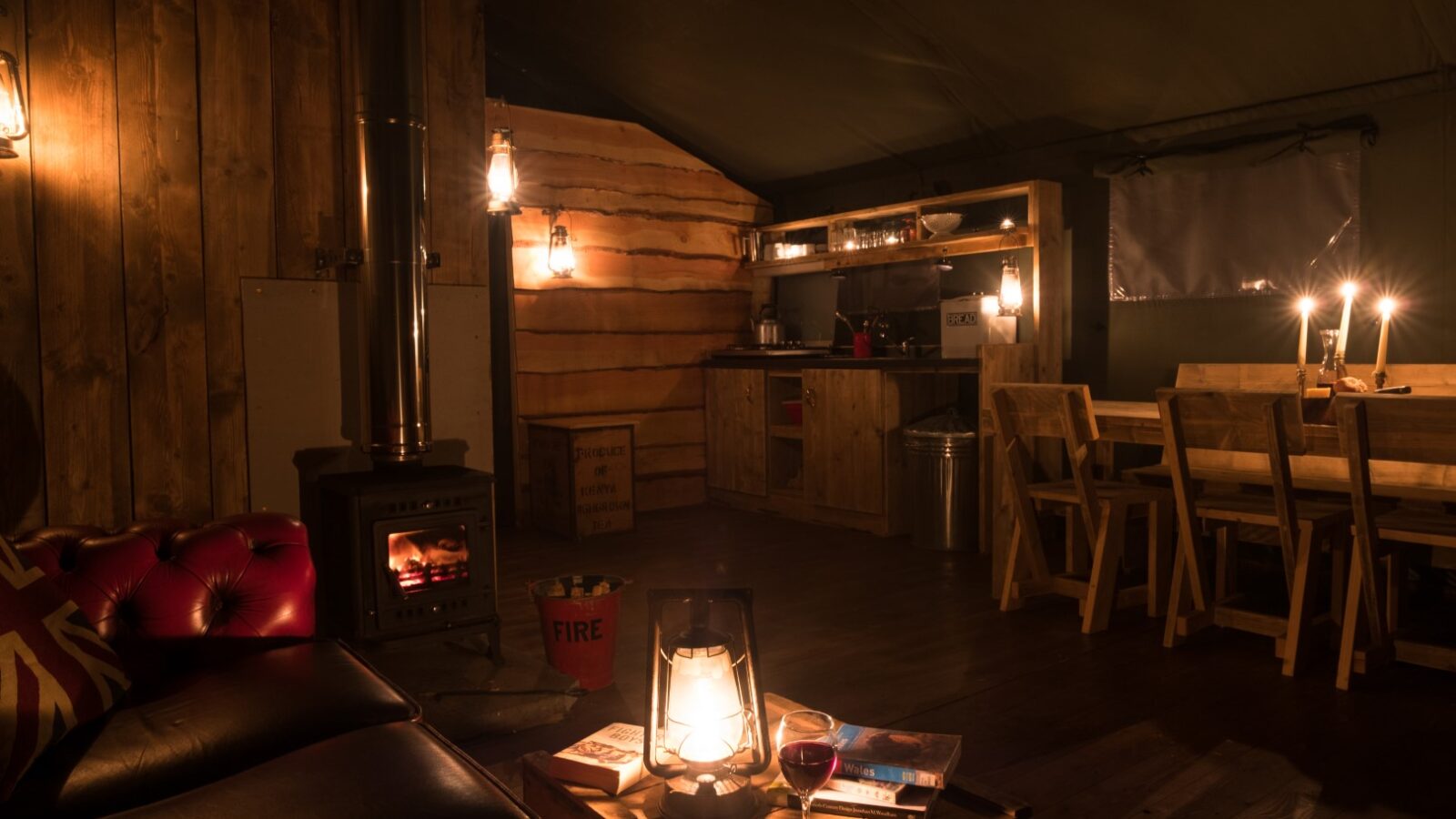 Nestled in the heart of Sloeberry Farm, this lodge offers a cozy cabin interior with dim lighting. Enjoy the warmth of a wood stove as you sit at the dining table, savoring a glass of wine beside a softly glowing lantern.