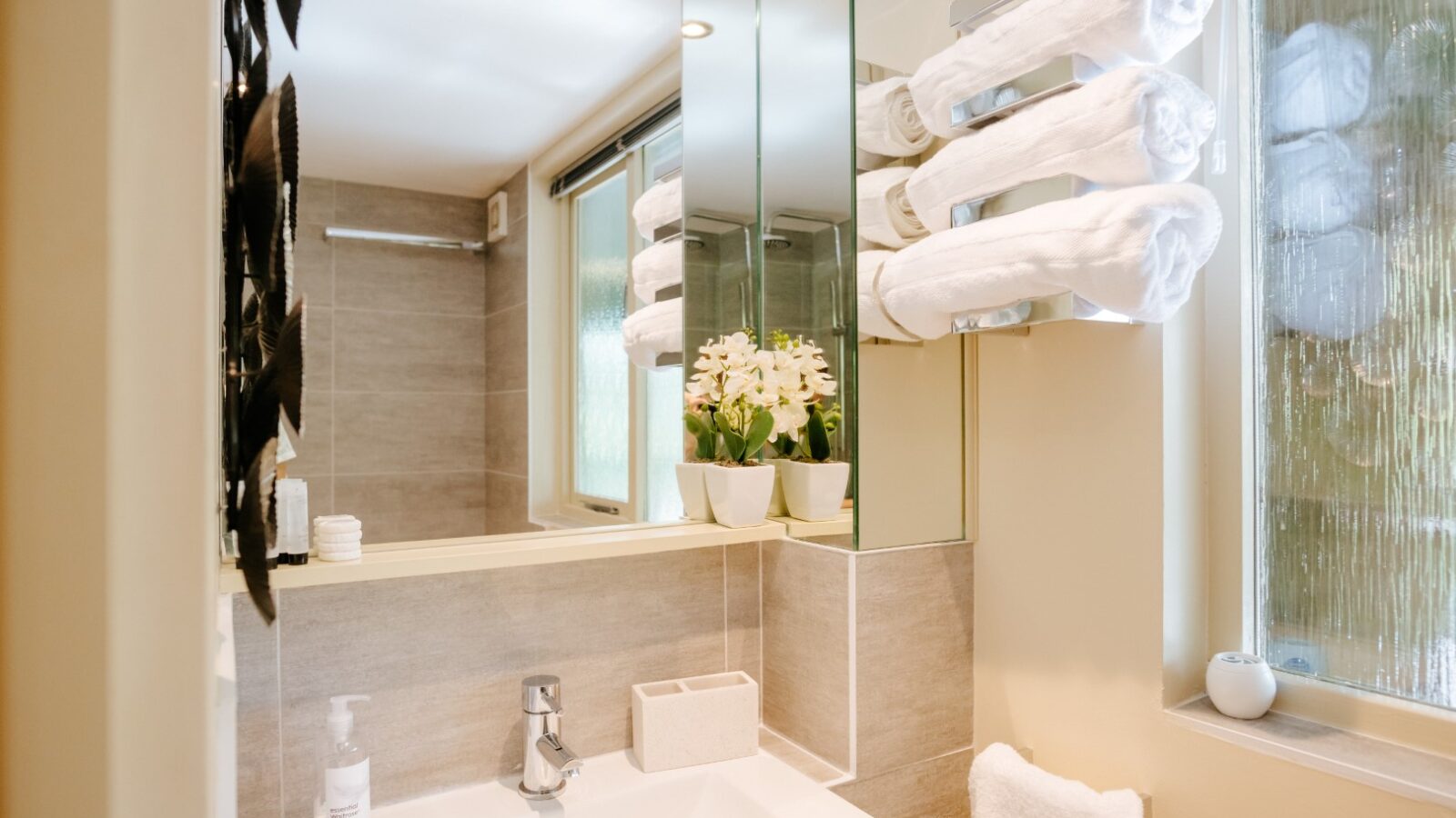 Modern bathroom with a sink, mirror, stacked white towels, and small potted plants on the counter, reminiscent of a tranquil retreat you'd find in Wills Treehouse.