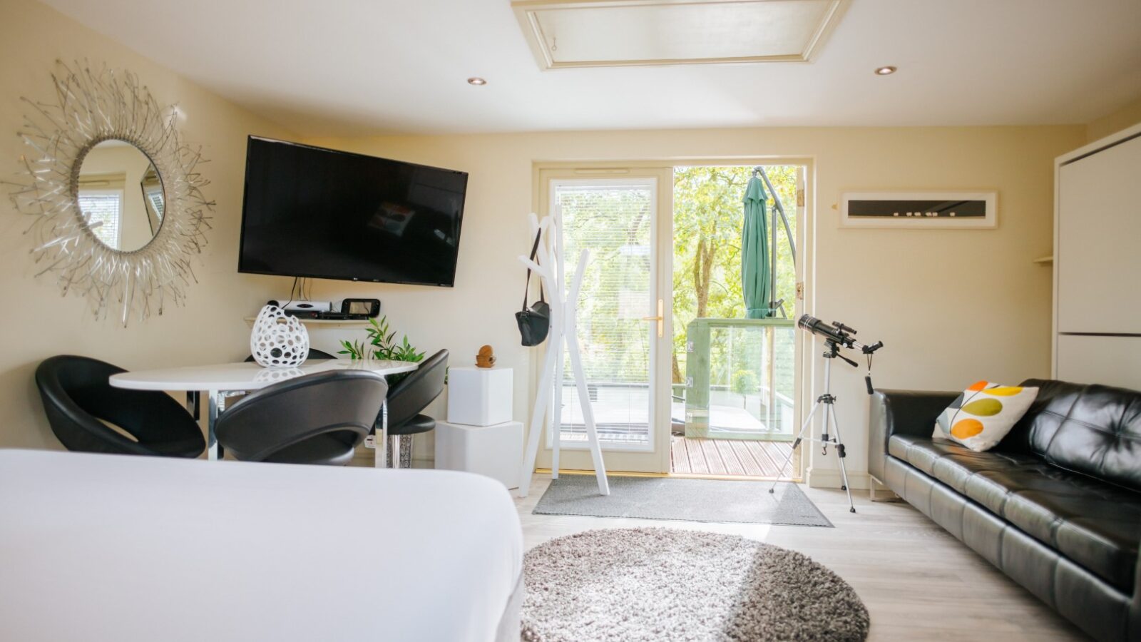 Bright, modern living space reminiscent of Wills Treehouse, featuring a cozy sofa, TV, round rug, and telescope by the glass doors that open to a balcony with inviting outdoor seating.