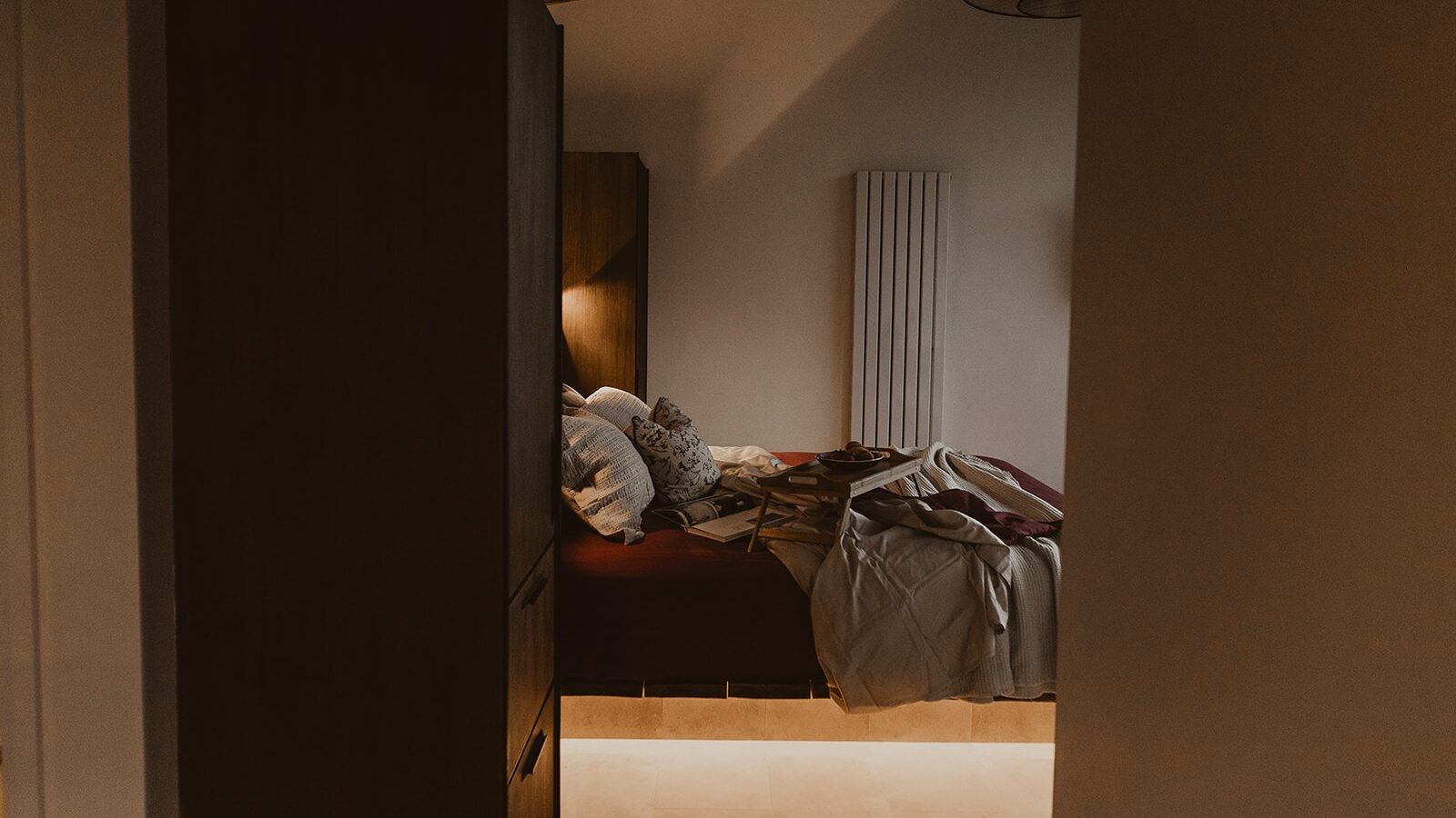 This cozy bedroom at Berry Bush Lodge features a wooden ceiling, a bed swathed in pillows and blankets, and a wardrobe partially visible on the left, offering charming accommodation for a restful getaway.