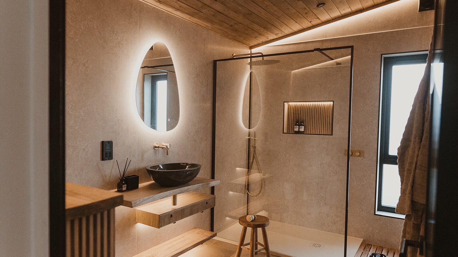 Modern bathroom at Berry Bush Lodge with wood accents, illuminated mirror, black basin, and a walk-in shower featuring a glass partition and wall niche.