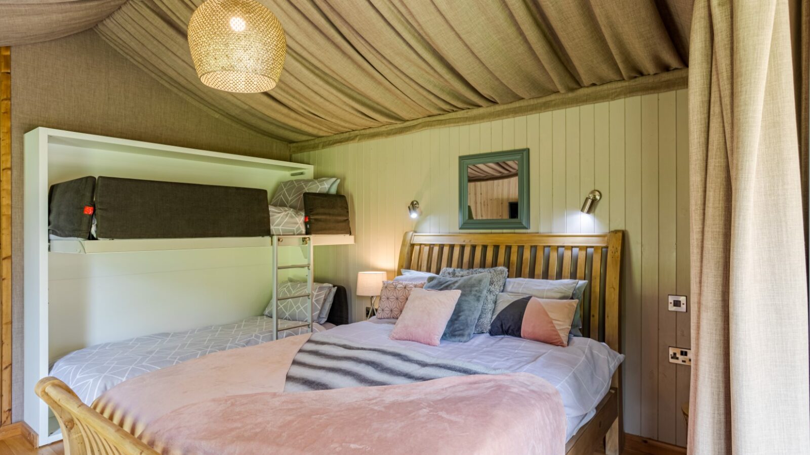 Cozy riverside bedroom with a double bed, bunk bed, decorative pillows, and soft lighting under a draped ceiling, reminiscent of charming cabins.