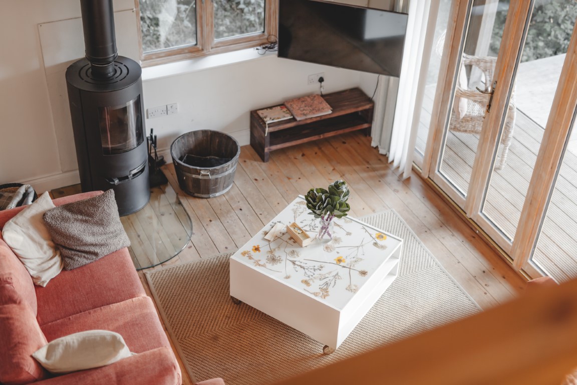 A cozy living room from Secret Escapes features a red sofa, wood-burning stove, white coffee table, and large windows overlooking a wooden deck—perfect for those dreamy Browning Bros gatherings.