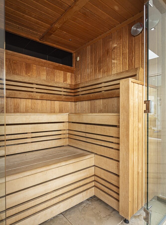 A wooden sauna room with tiered benches and a glass door, reminiscent of the cozy charm found in Cary Arms suites, featuring clean lines and natural light from an unseen source.