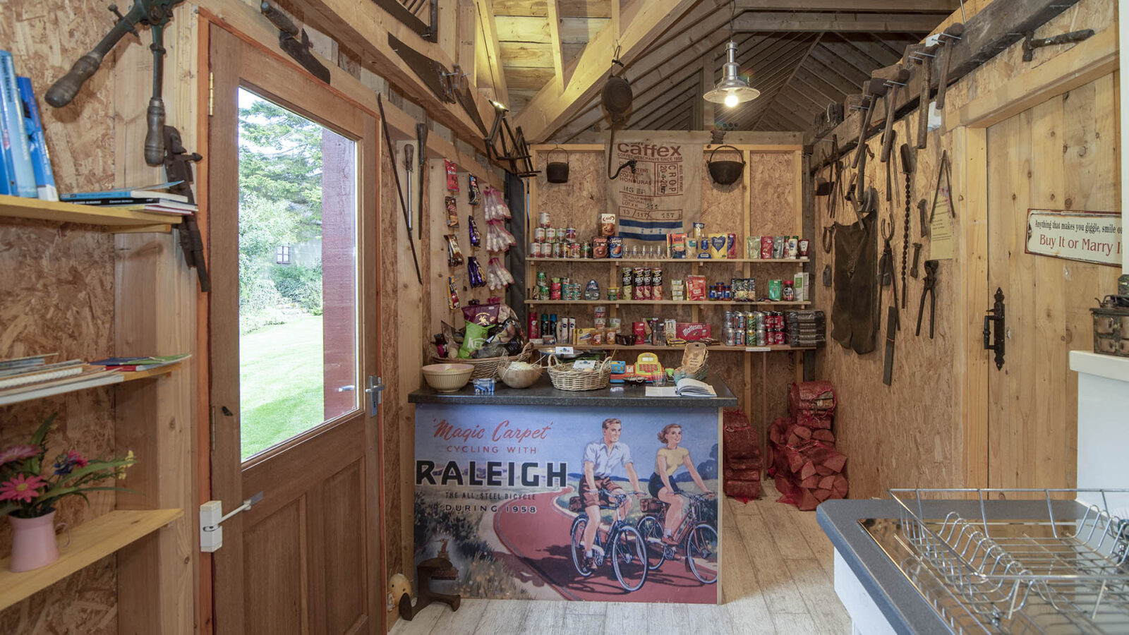 Nestled in a cozy wooden shed, Craighead Howf offers an eclectic mix of snacks, drinks, and cycling gear. A vintage Raleigh poster adorns the wall, adding charm to this unique locale.