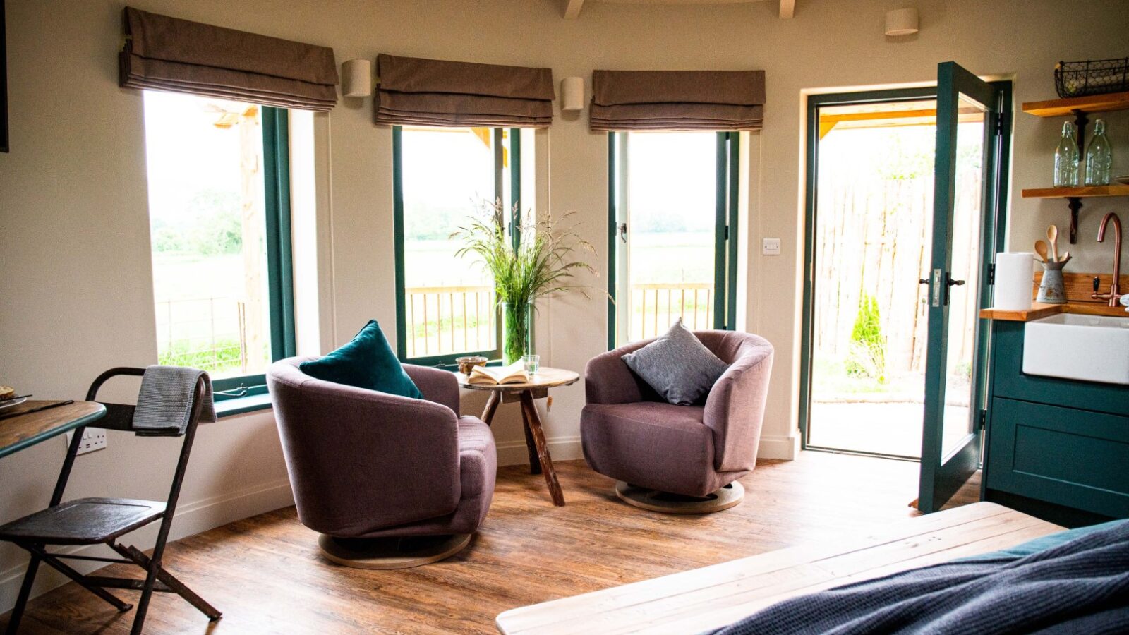 Cozy living area with two armchairs, a small table with flowers, and large windows, creating the perfect retreat. The door opens to an outdoor view, inviting relaxation after finishing the laundry.