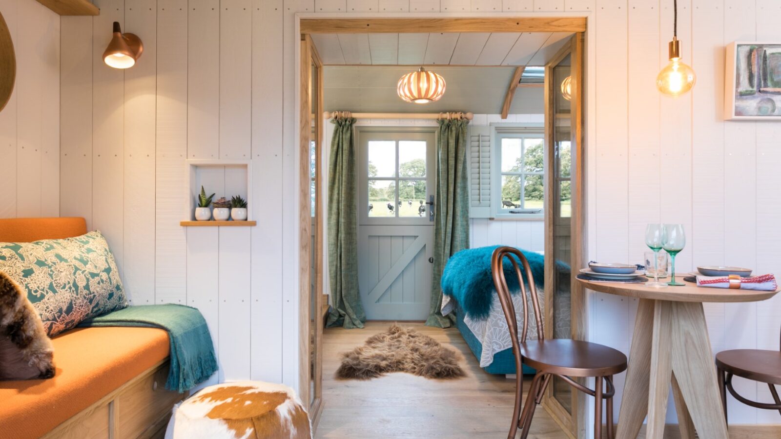 Cozy interior with a small dining table, chairs, and bench seat, offering a charming Dimpsey vibe. Enjoy the picturesque view into a bedroom with easy glamping access through the door leading outside.