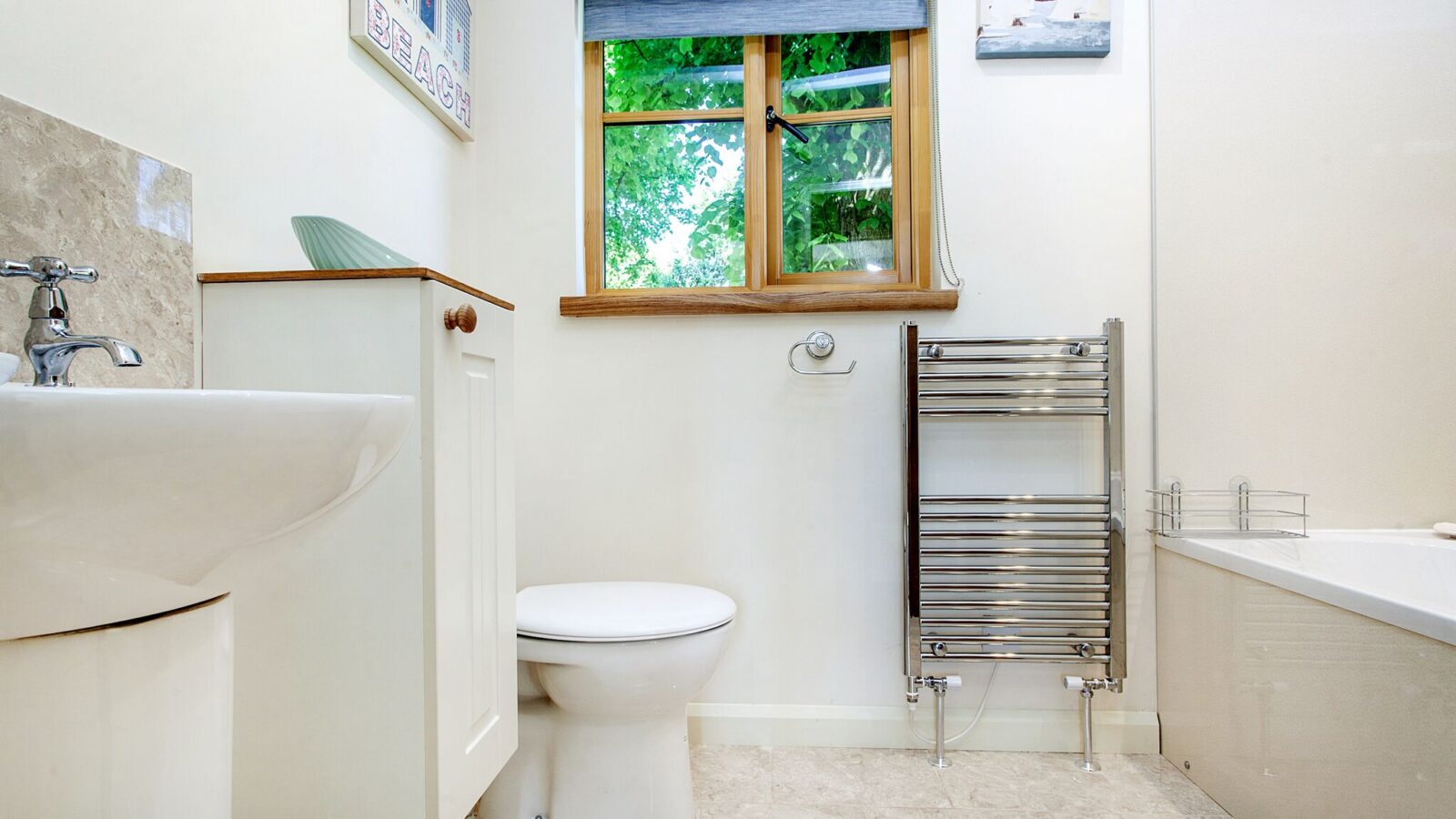 A modern bathroom on Lavender Hill features a toilet, sink, wall-mounted towel rack, window with treehouse views, artwork, and a corner of a bathtub.