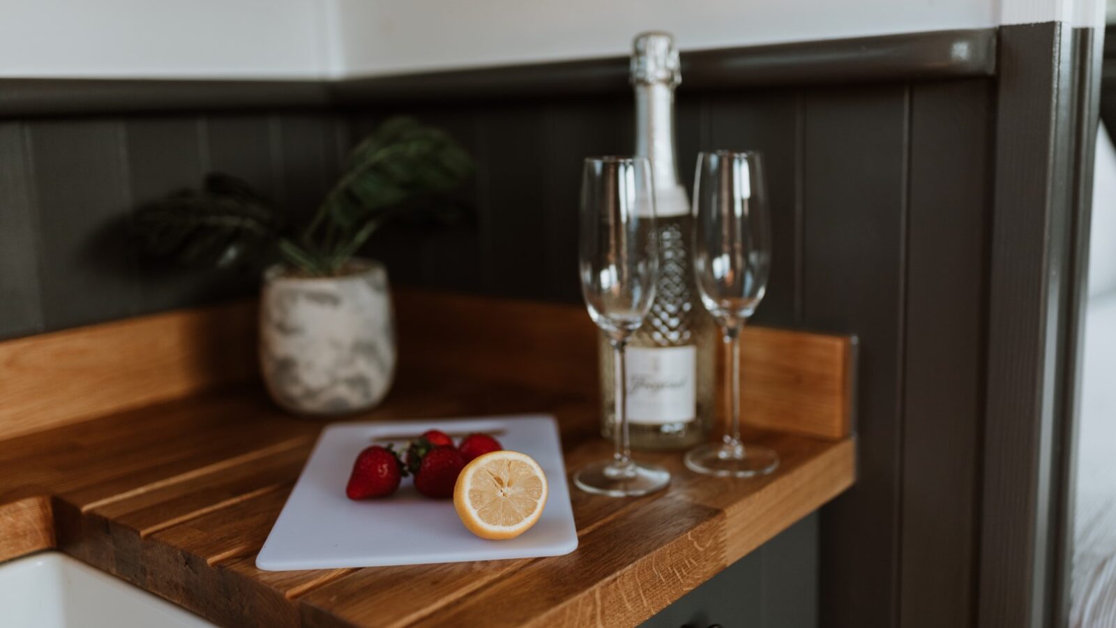 A rustic scene unfolds on a wooden counter: a cutting board adorned with strawberries and lemon slices, alongside a bottle of champagne and two glasses, evoking memories of a serene retreat in a Shepherd's Hut.