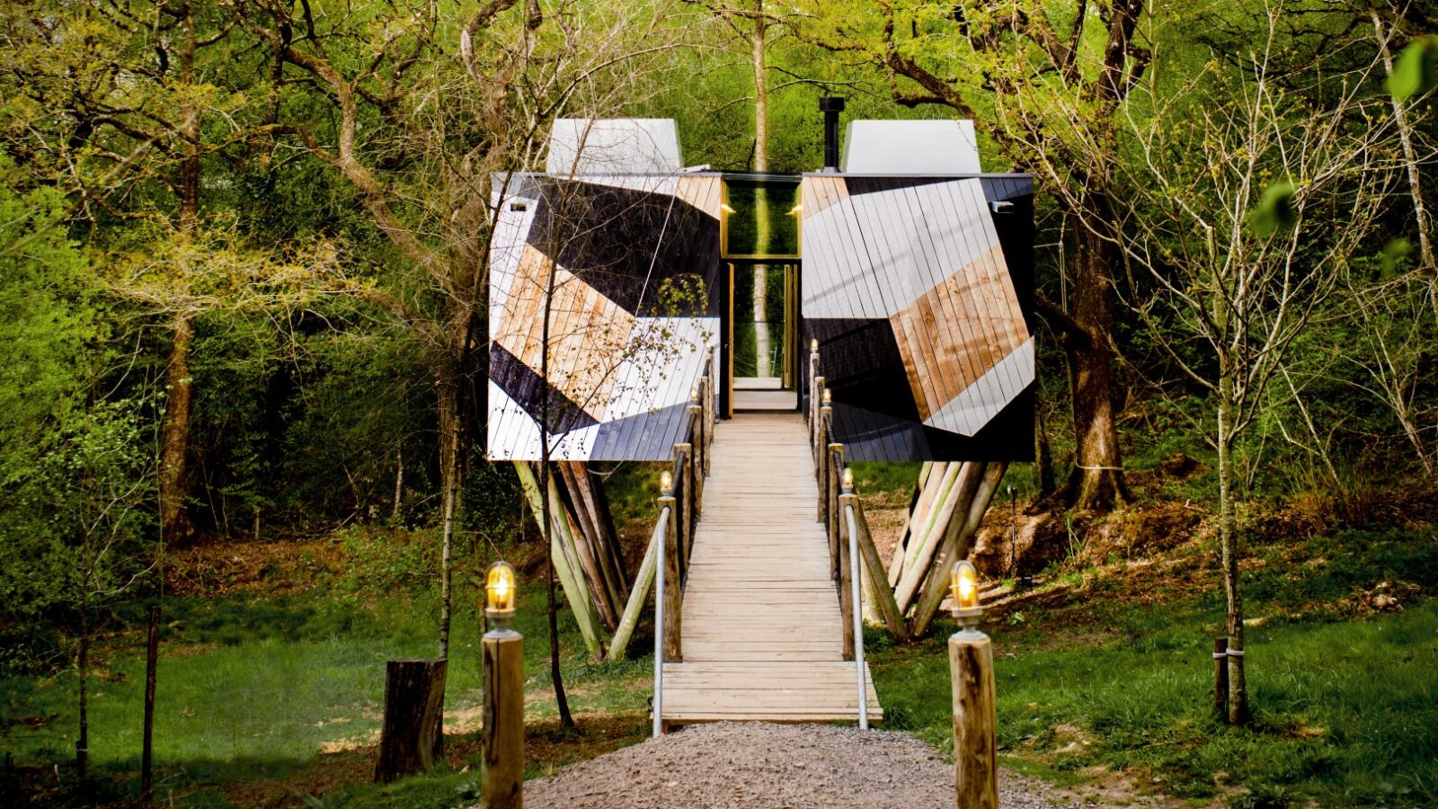 The Dazzle Treehouse, a modern geometric marvel, features a walkway that meanders through lush green forest under a clear sky.