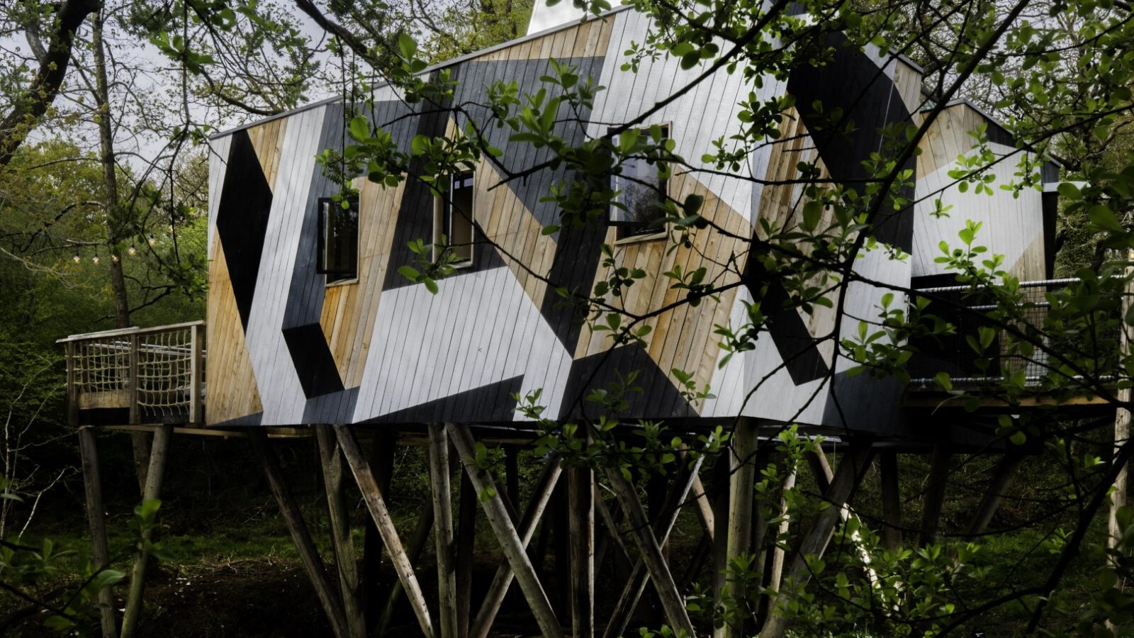 Experience the Dazzle Treehouse, a modern retreat elevated on stilts among lush greenery, showcasing striking geometric wood patterns that blend seamlessly into the forest canopy.