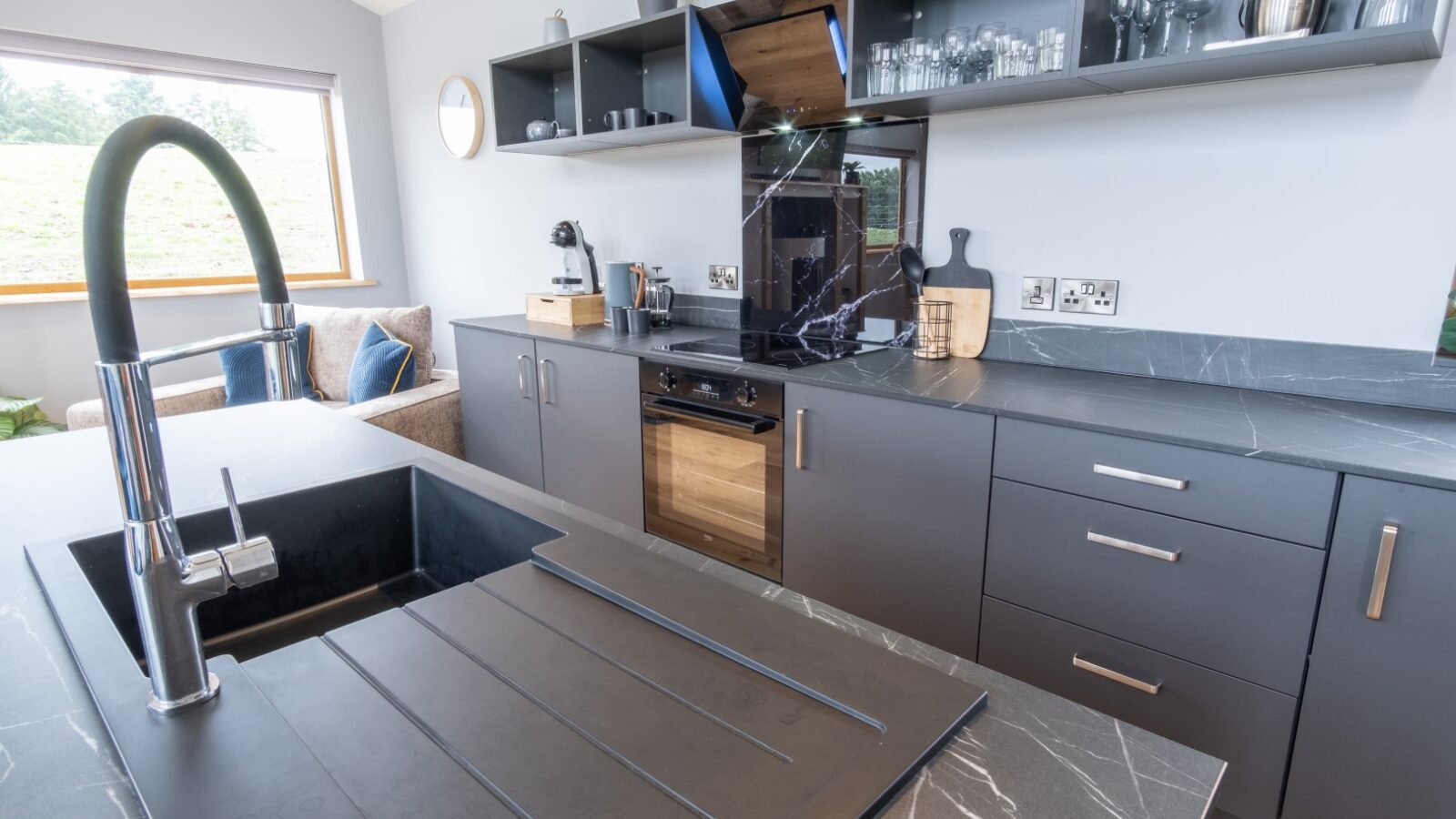 Discover a modern kitchen where dark cabinets and black marble countertops seamlessly blend with a built-in oven. A matte black faucet graces the central island, embodying the sleek elegance that Lodges aspire to match.