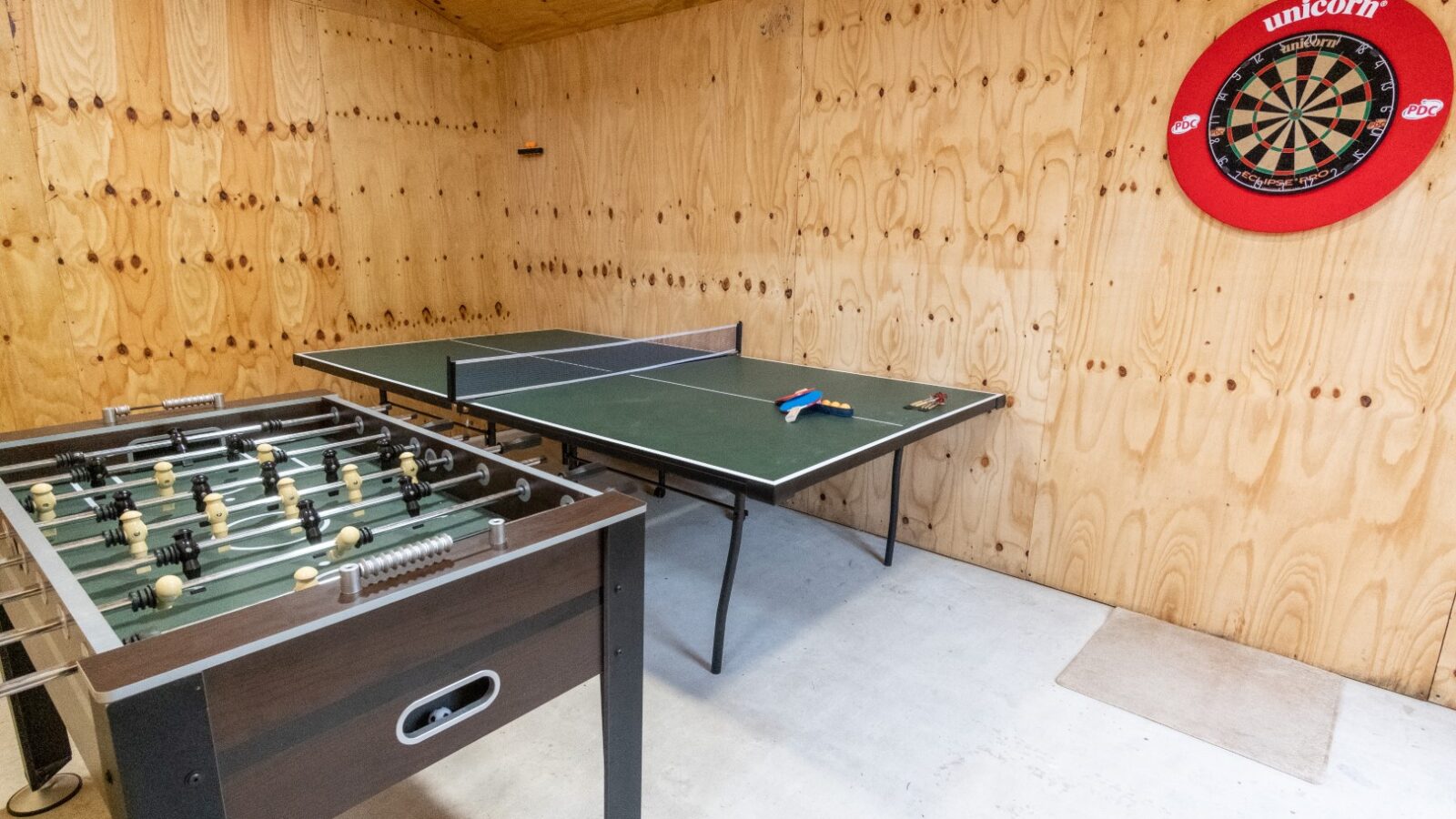 This Lundy lodge features a lively room equipped with a foosball table, a ping pong table complete with paddles and balls, and a dartboard mounted on the wooden wall. Perfect for those seeking entertainment and relaxation.