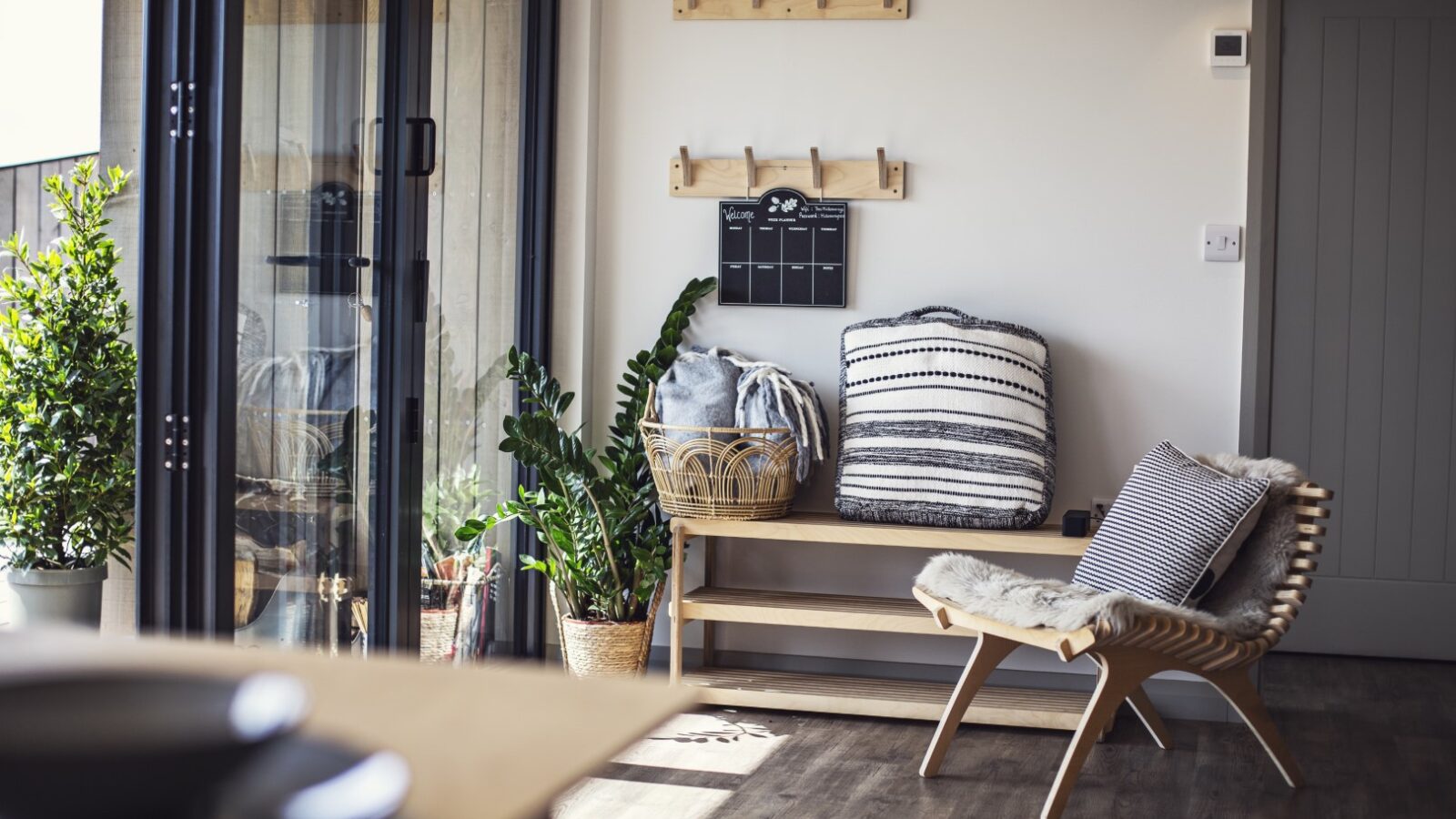 Cozy hideaway featuring a wooden chair, striped pillows, plants, a Pontypinna wall calendar, coat hooks, and large glass doors opening outside.