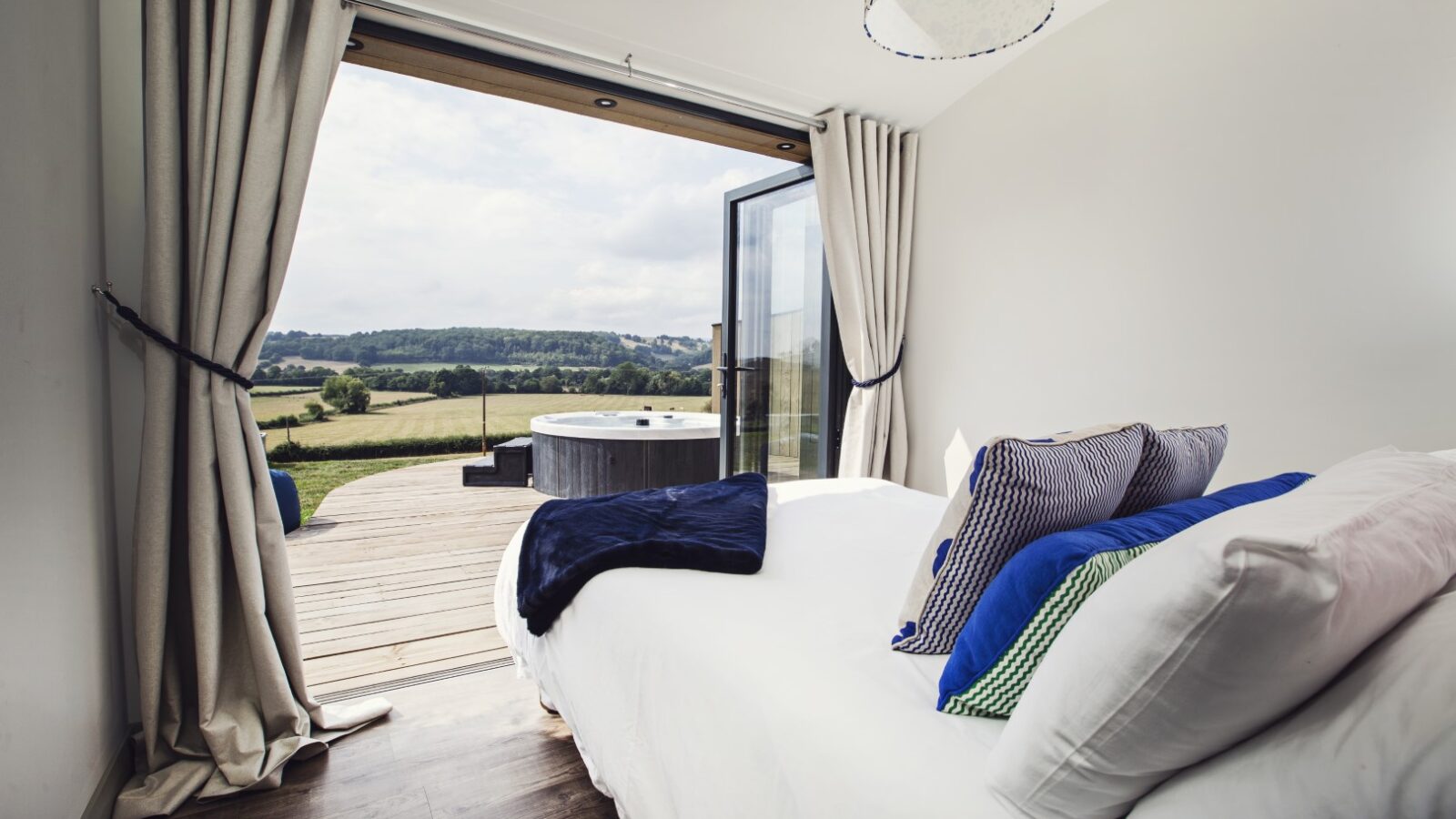 A bedroom with open sliding doors overlooks the serene Pontypinna countryside, featuring a patio with a hot tub and deck chairs—a perfect hideaway.