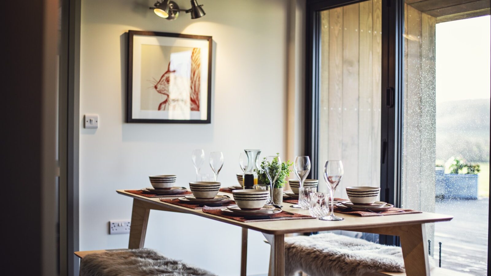 Dining table set for a meal, featuring plates, glasses, napkins, and a stunning centerpiece in a cozy Pontypinna hideaway, with fur-covered benches adding warmth and charm.