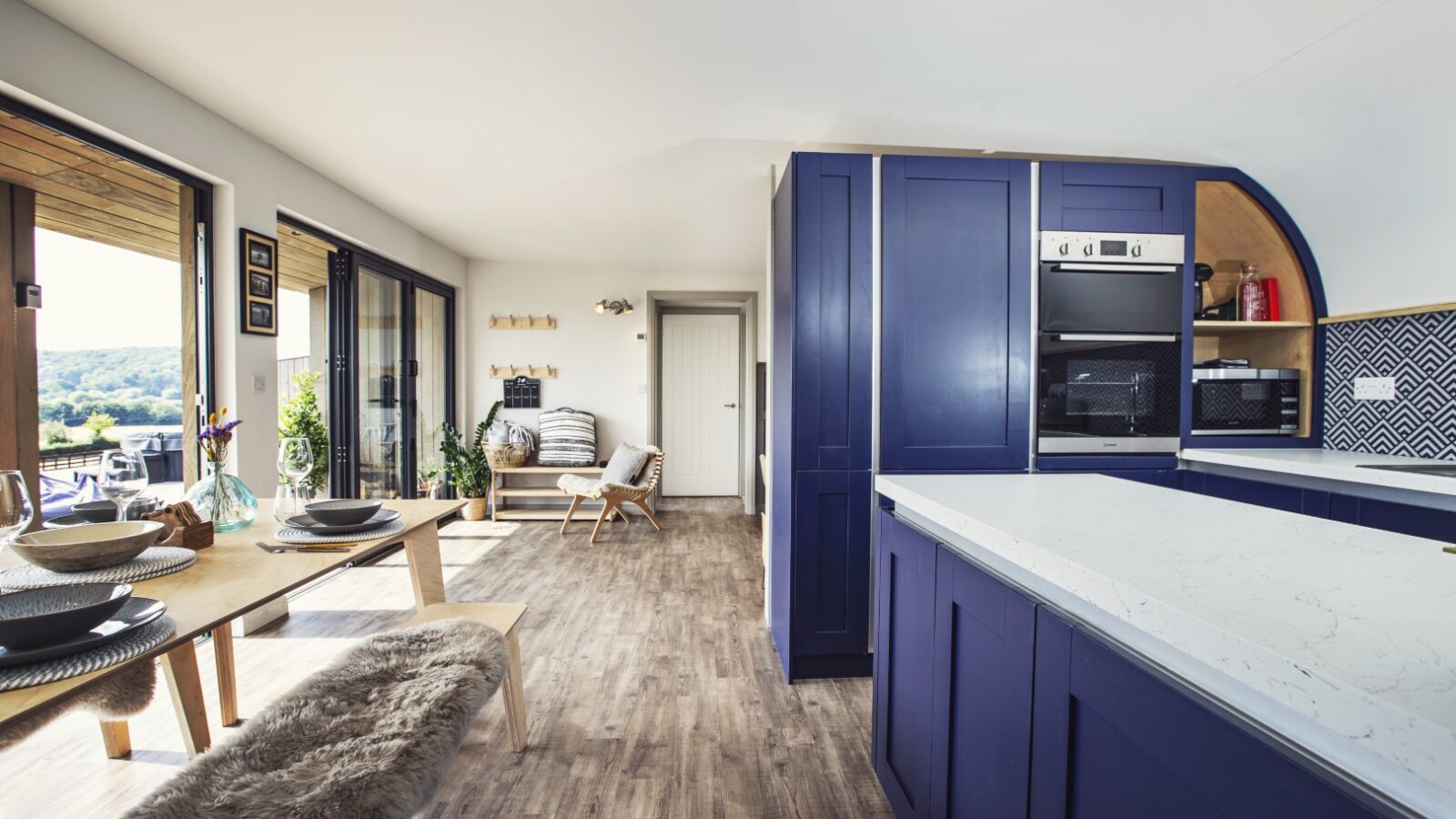 Discover a modern kitchen in Pontypinna, featuring blue cabinets and a dining table with bench seating. Large windows offer serene views of the outdoors, perfect for secluded hideaways.