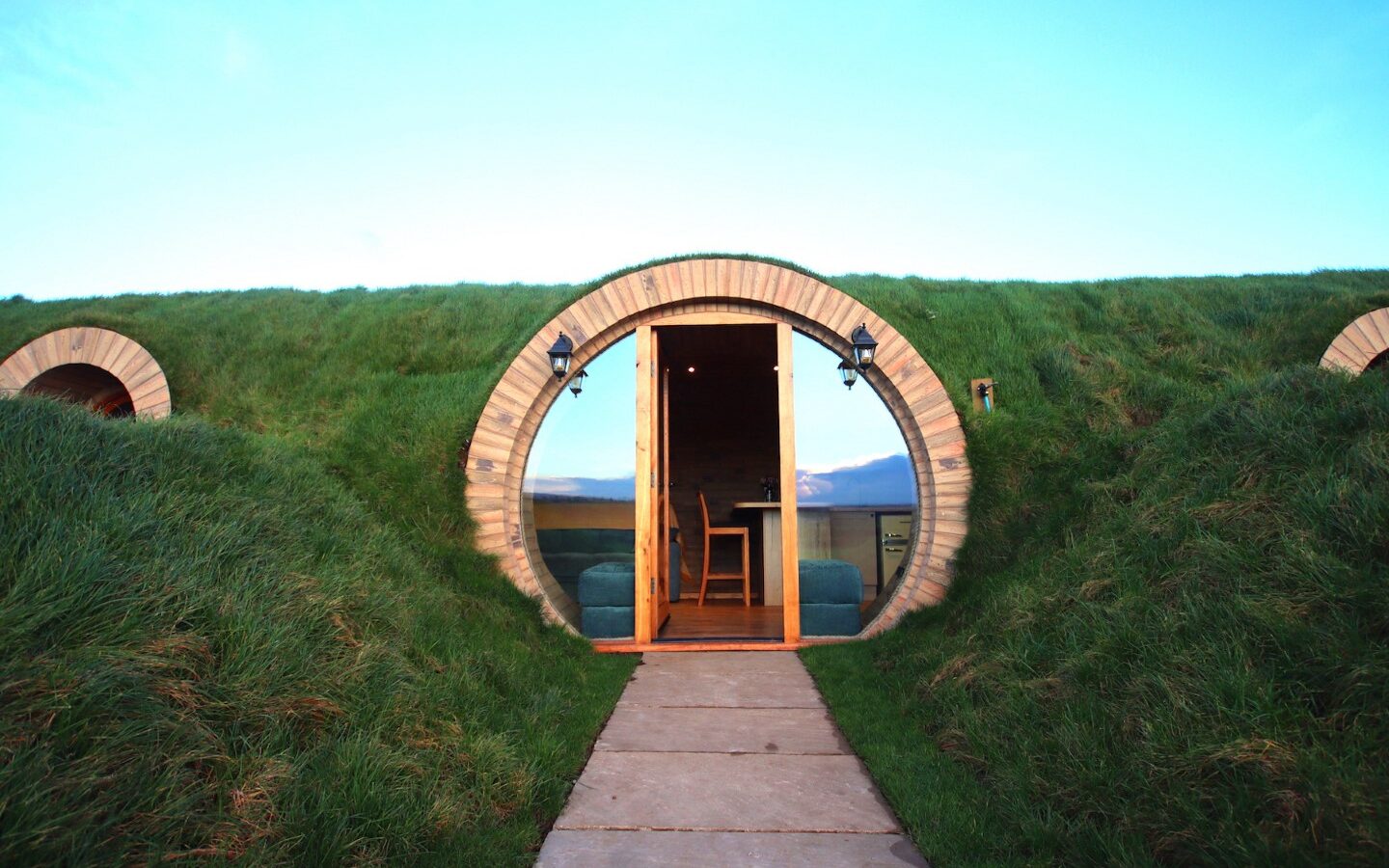 A circular wooden entrance nestled in a grassy Yorkshire hillside, resembling a hobbit house, with a winding path leading to an open door, reminiscent of cozy burrows.