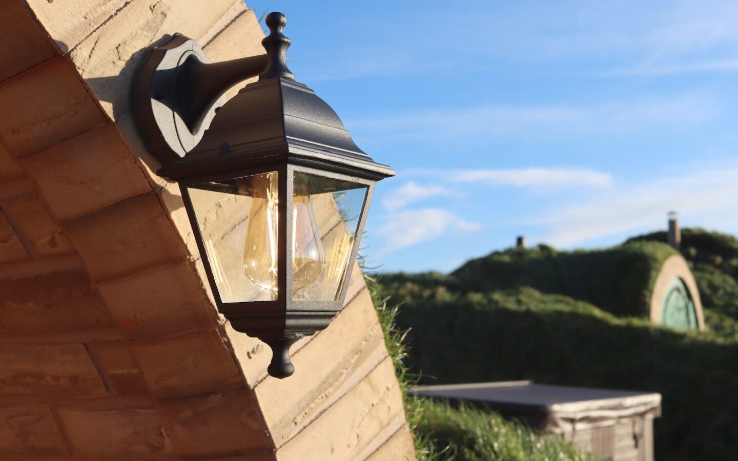 Black lantern on an arched brick wall with grass-covered roofs of Yorkshire Burrows in the background, all under a clear blue sky.