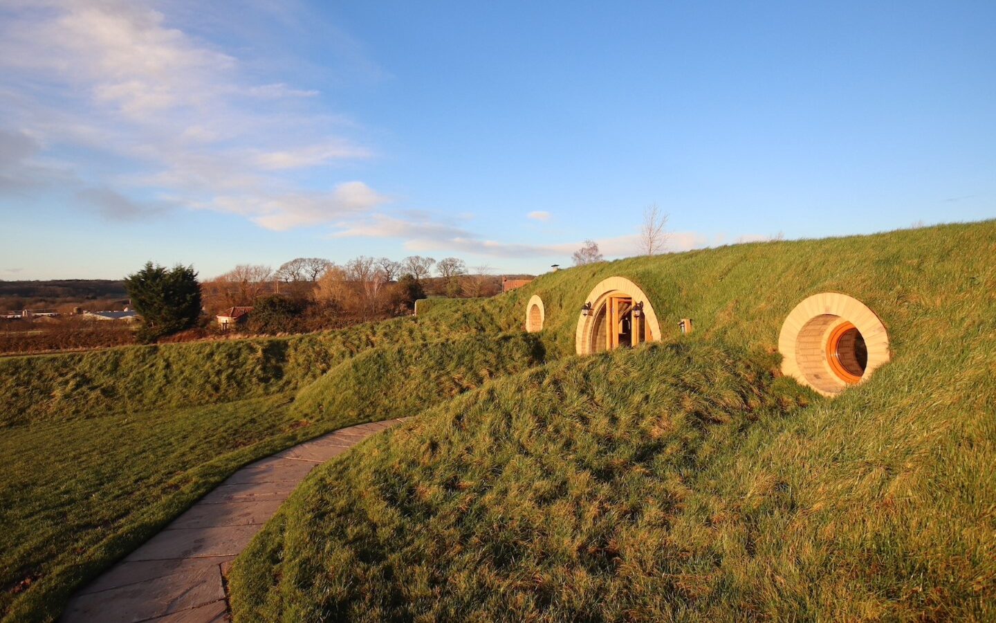 A grassy landscape reminiscent of Yorkshire, with round door homes built into small burrows under a clear blue sky.