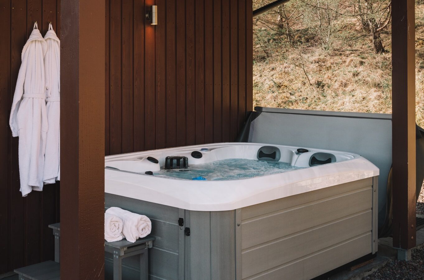 Outdoor hot tub under a wooden gazebo with towels and robes hanging on the wall, perfect for unwinding and sketching in your drawing pad.